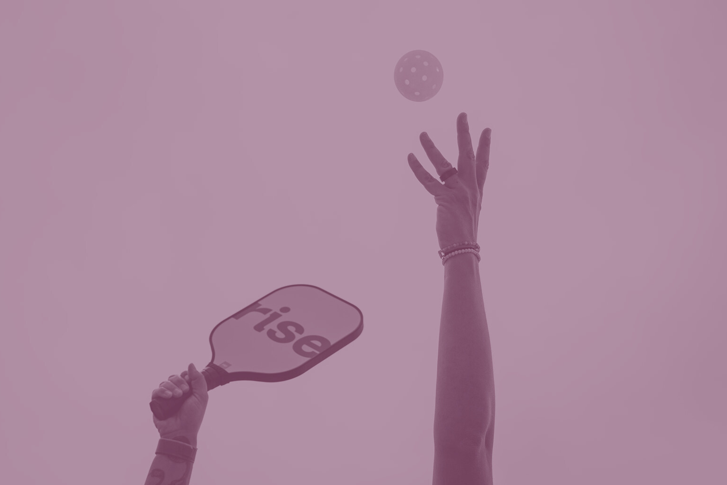 A person holding a table tennis paddle with the word 'ise' on it, and a hand reaching up to hit a ball in the air.