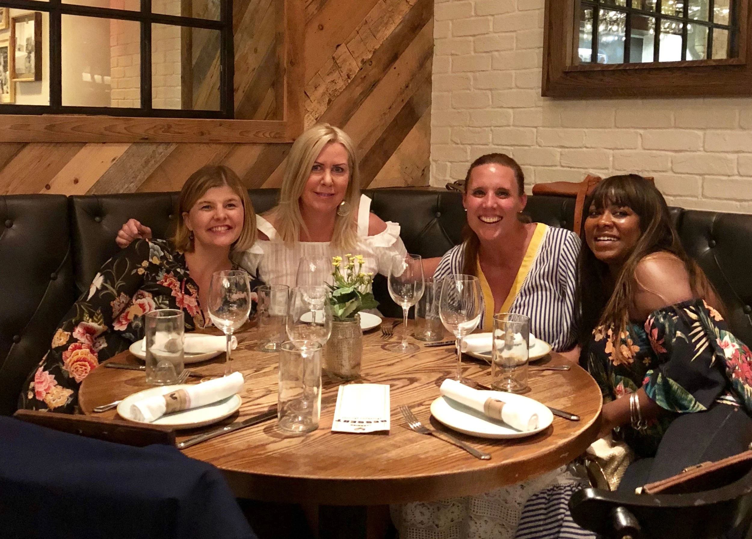 Four women sitting at a round dining table in a restaurant, smiling.