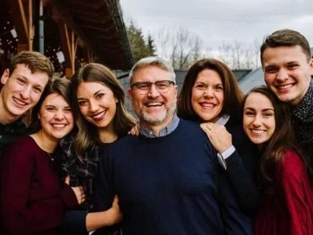 Family of seven gathered outdoors, smiling and posing for a group photo.