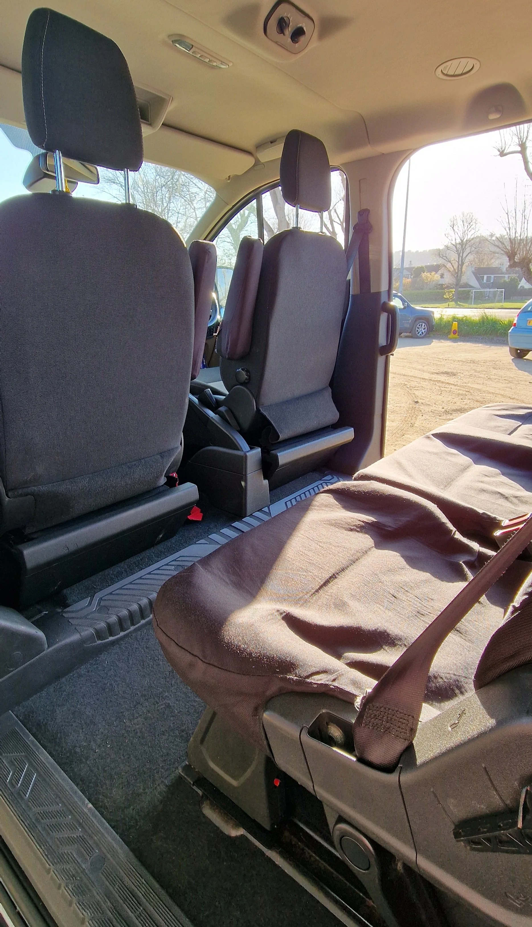 Interior of a vehicle showing four seats, three upright and one with a harness, with sunlight coming through the windows.