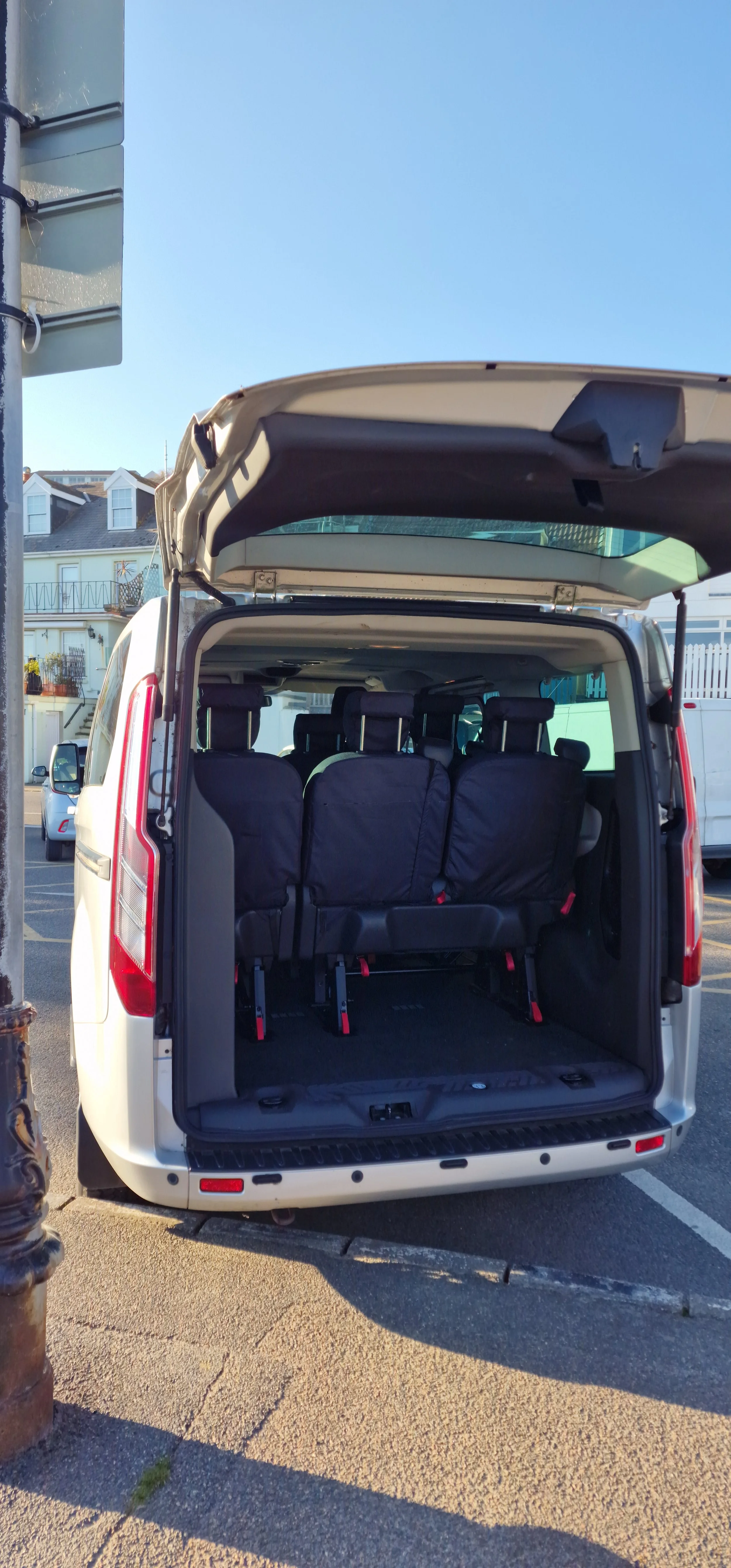 The rear of a white van with the back door open, showing three folded seats inside.