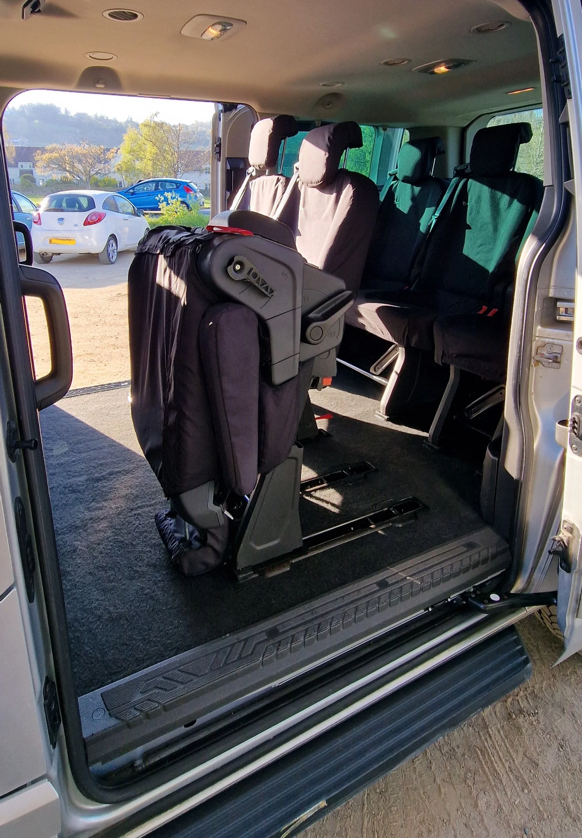 Interior of a wheelchair-accessible van showing a foldable seat and empty rows of seats, with an open side door.