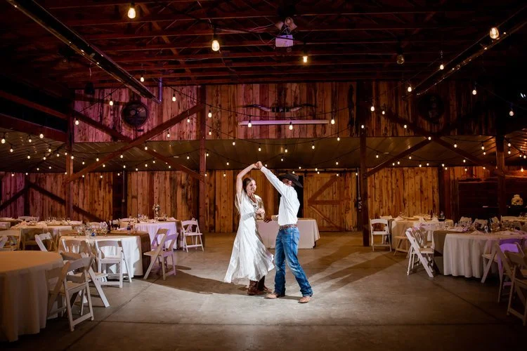 A couple dancing in a rustic barn wedding venue with wooden walls and string lights