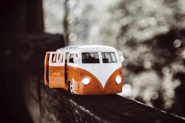 Toy model of a classic orange and white van with open doors on a wooden surface outdoors.
