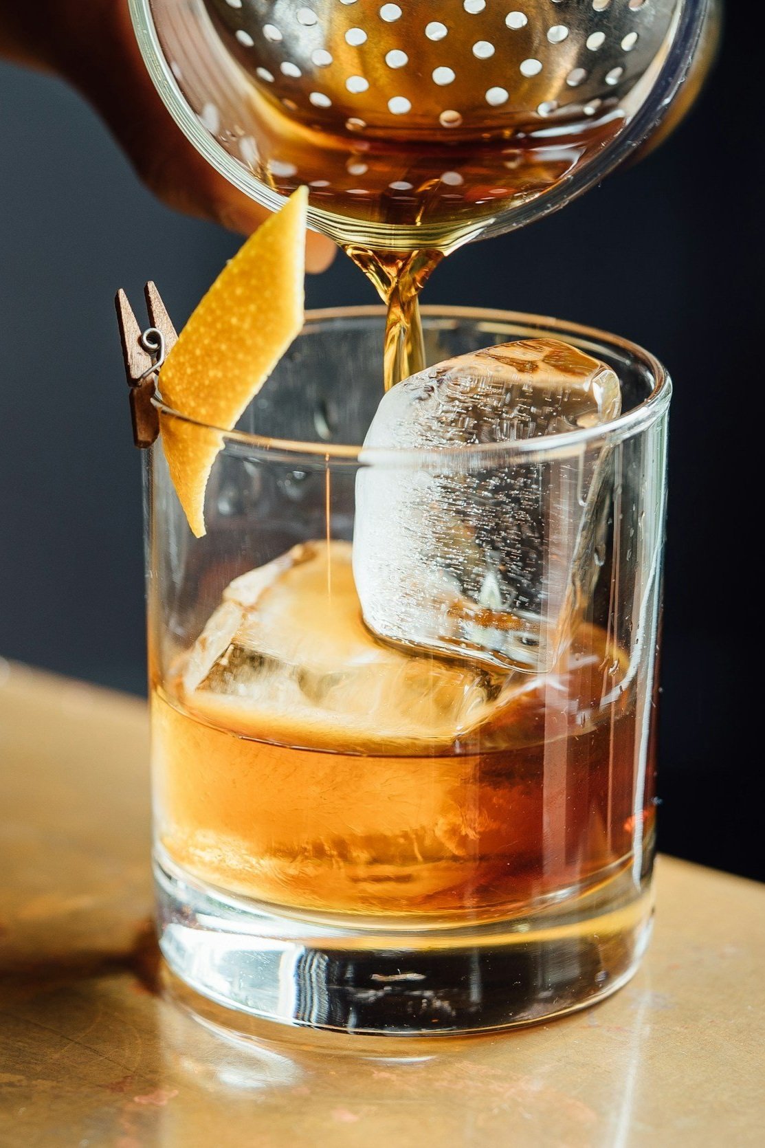 Whiskey being poured into a glass with ice cubes and garnished with an orange peel.