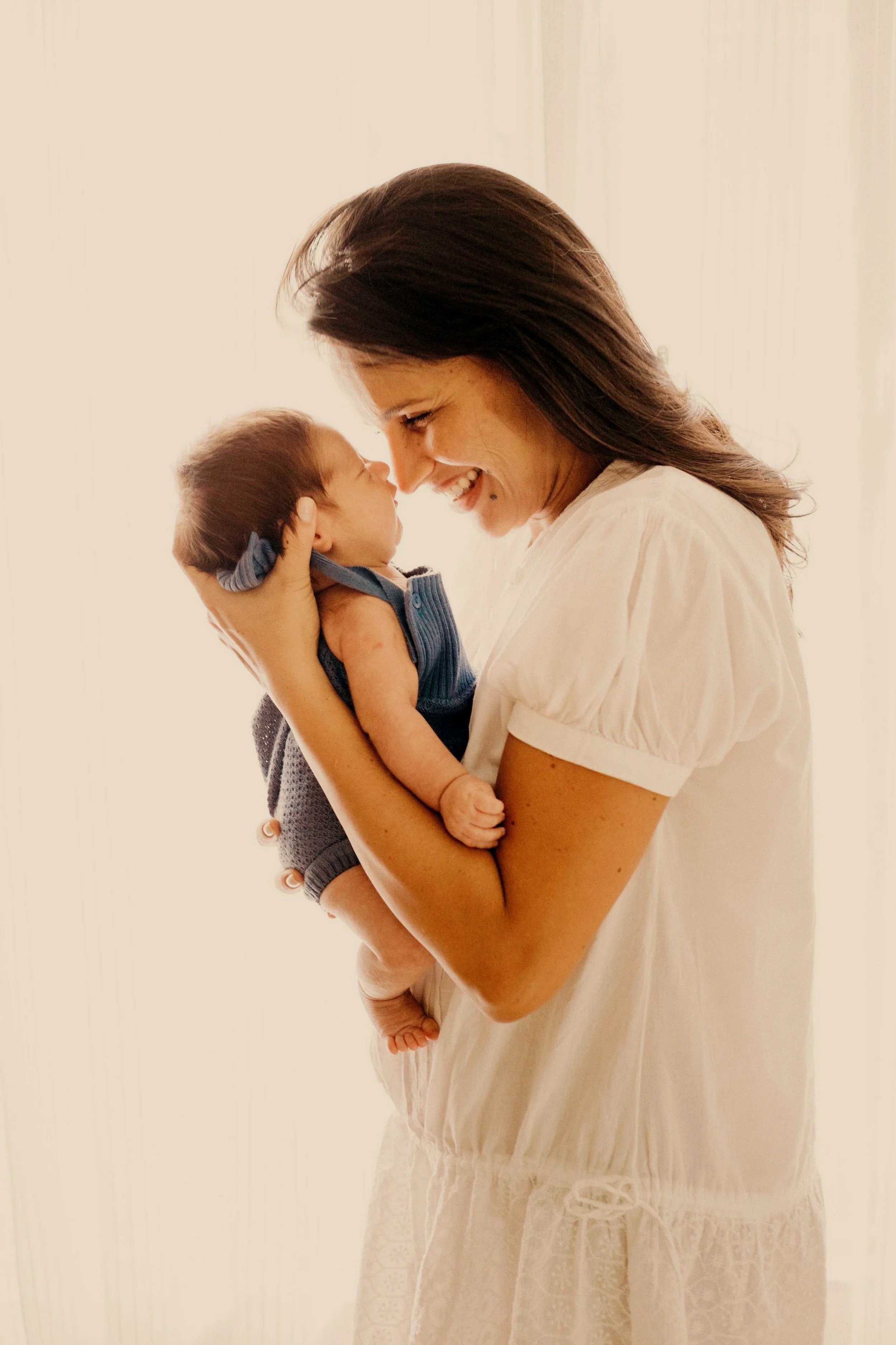 Smiling mother holding her newborn baby close, nose to nose.