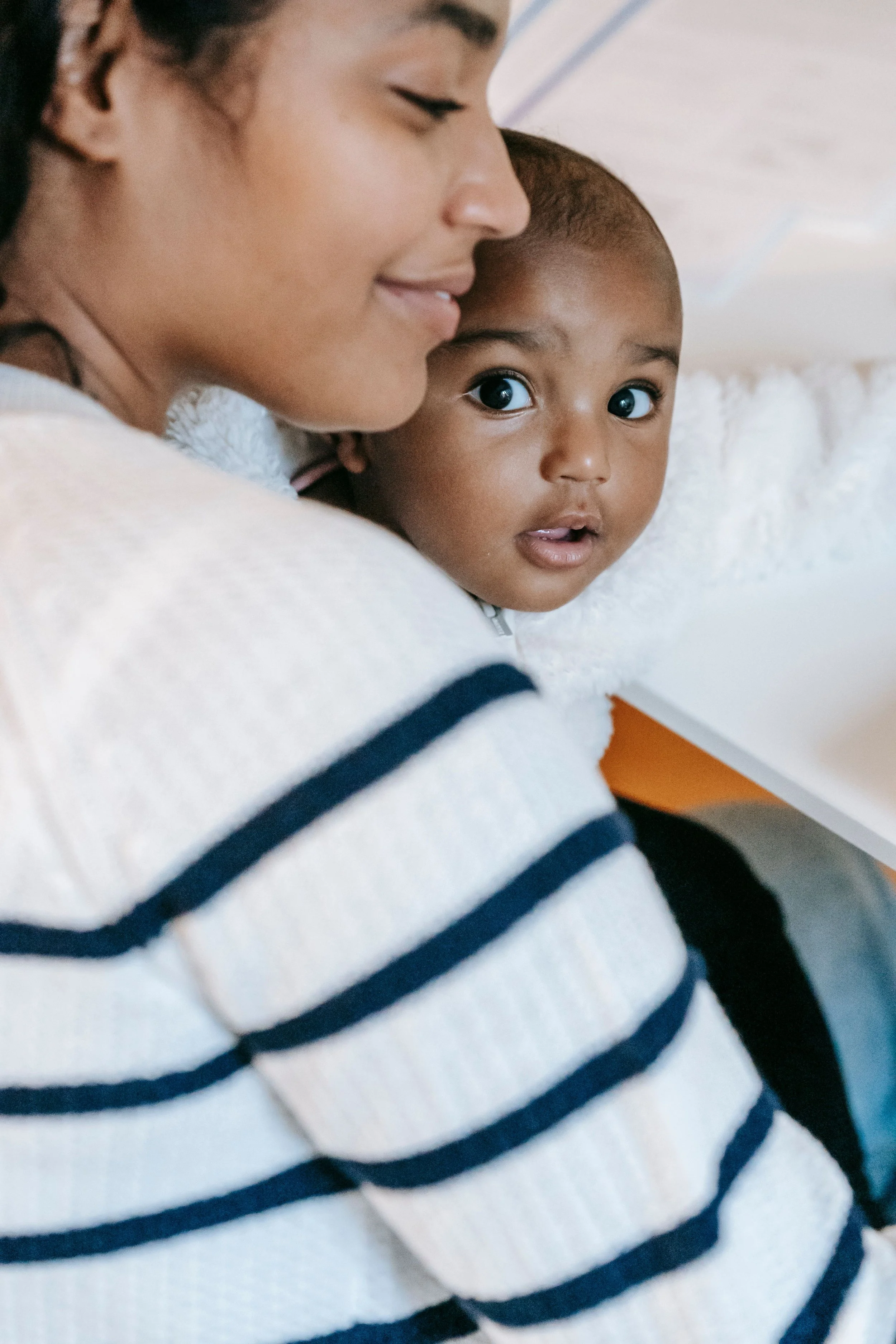 Parent cuddling a wide-eyed baby wrapped in a soft white blanket.