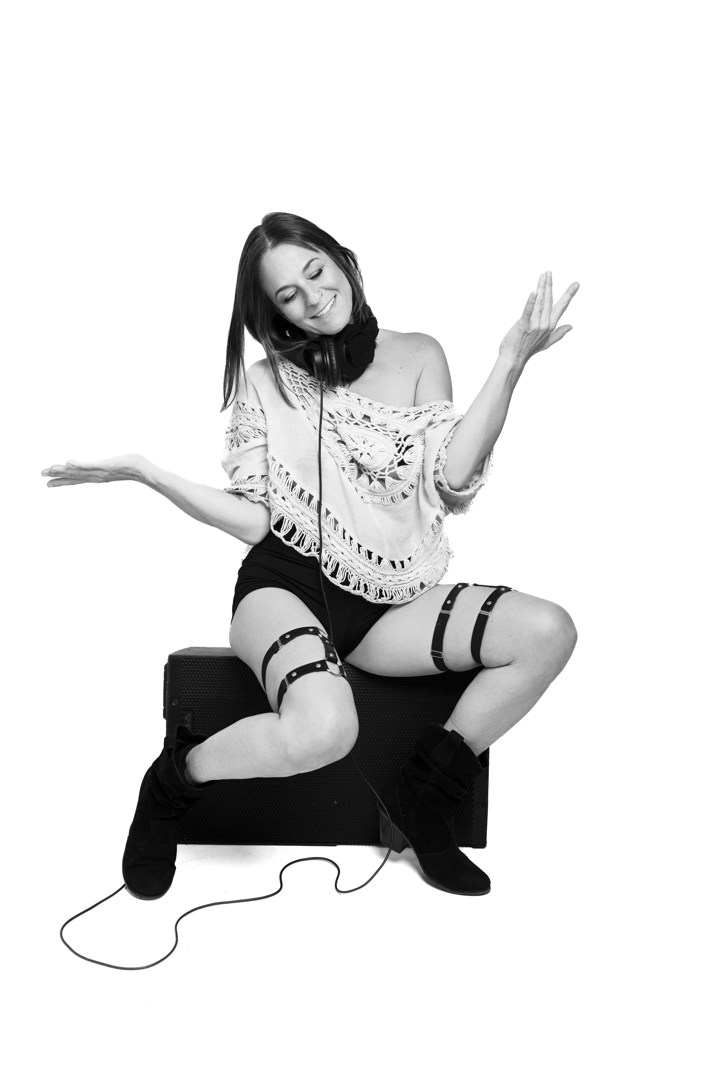 A woman dancing on an amplifier, wearing headphones, a lace top, shorts, garter straps, and boots, with a joyful expression.