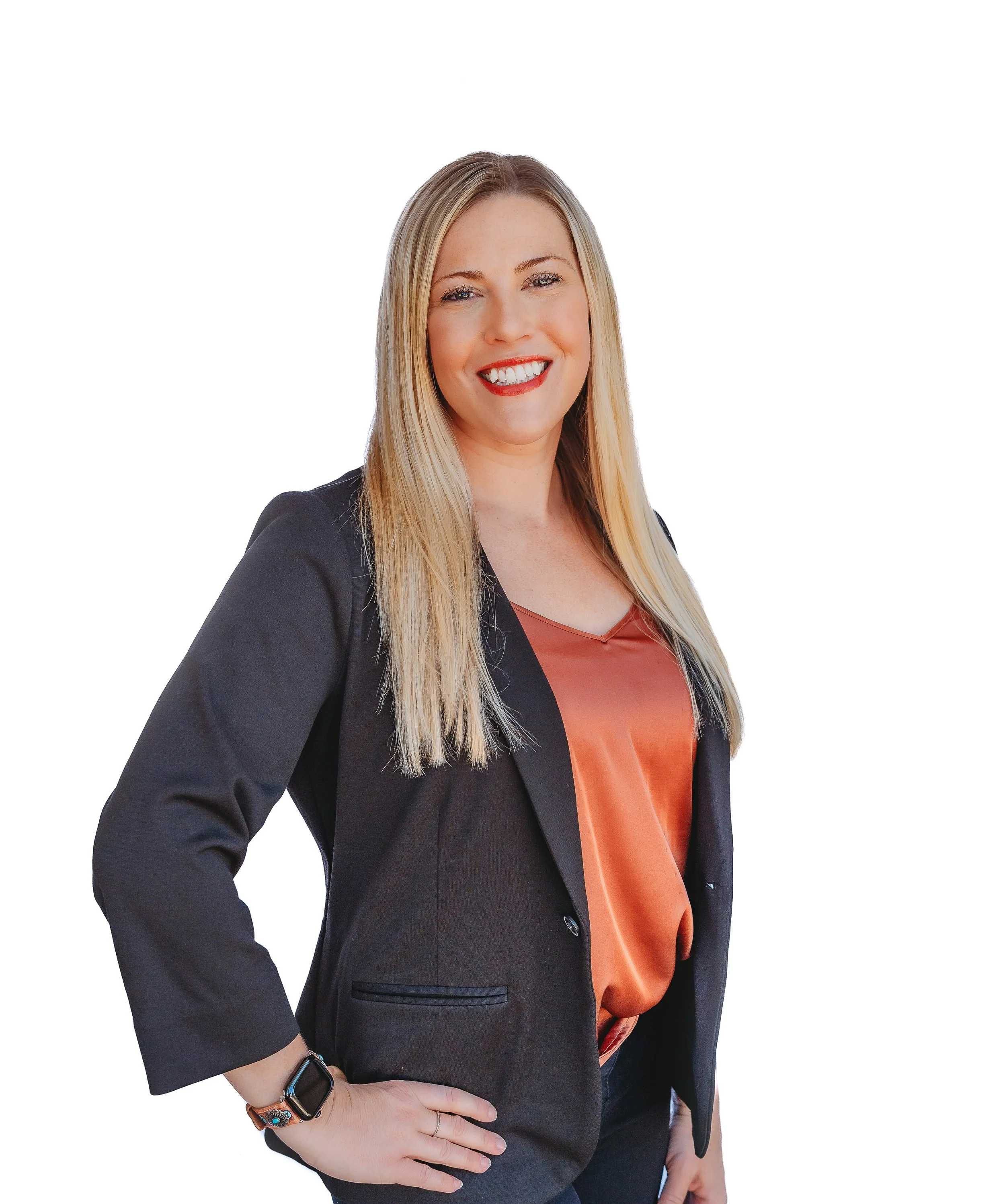 A woman with long blonde hair, smiling, wearing a black blazer over an orange satin blouse, with her right hand on her hip