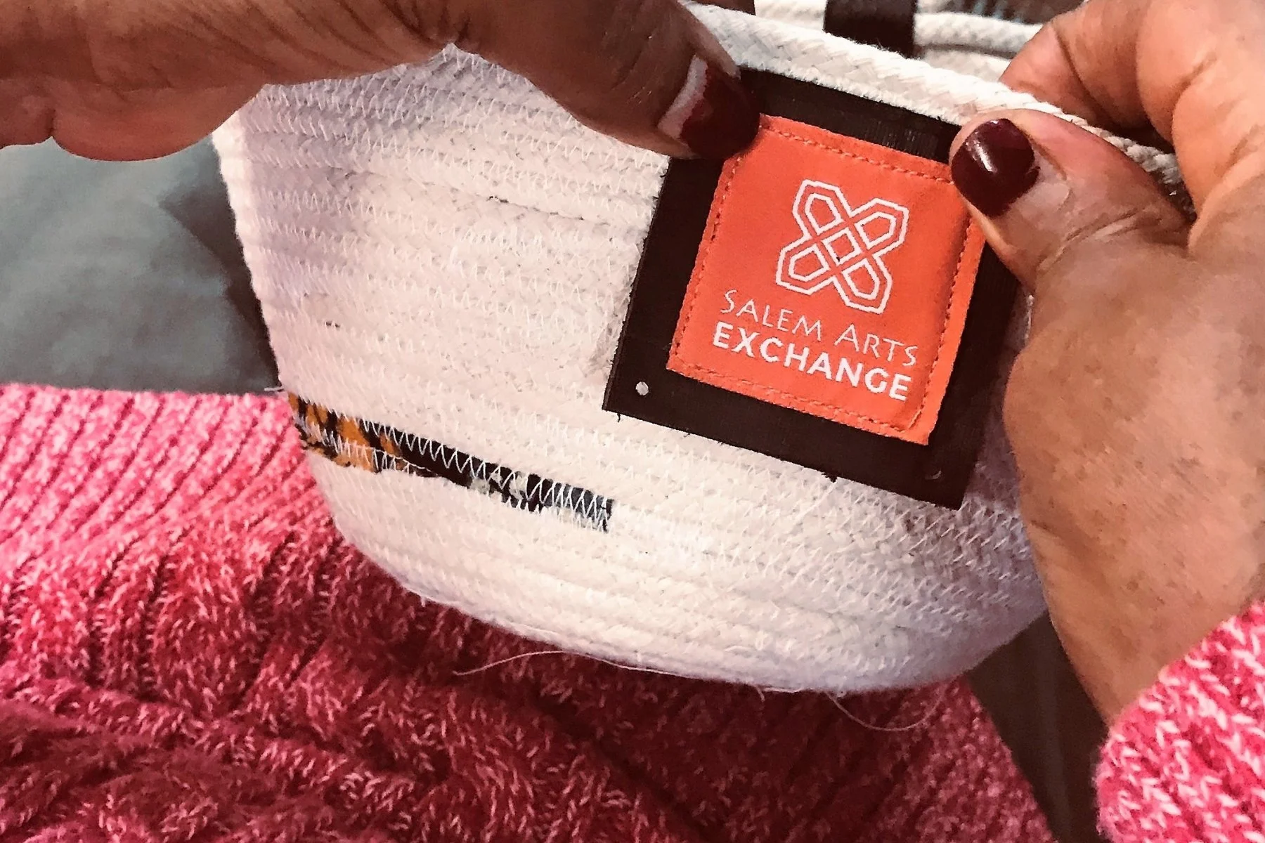 Close-up of a person's hands holding a white fabric bowl with a Salem Arts Exchange tag.