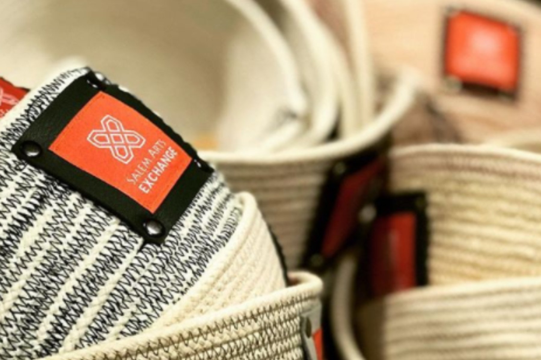Close-up of cloth bowls that are beige with a black squiggly design and have a black and orange tag that reads 'Salem Arts Exchange'.