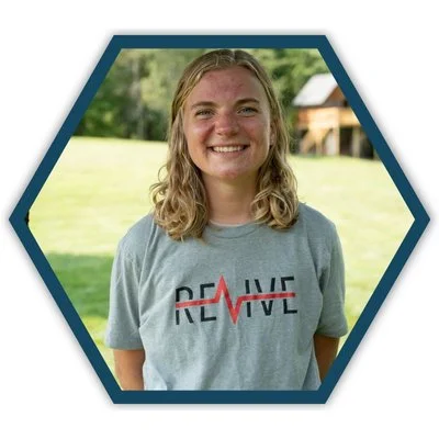 Portrait of Madison Kroes, a CityJoy staff member who works with Revive and mentors youth, smiling outdoors with a grass field in the background.