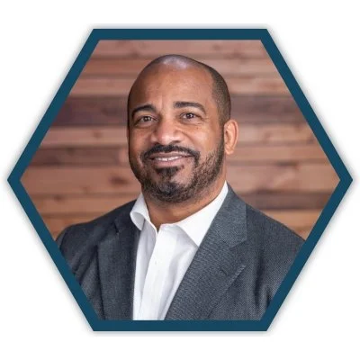Portrait of Dr. B. Charvez Russell, member of the CityJoy board of directors, smiling in front of a wooden background.