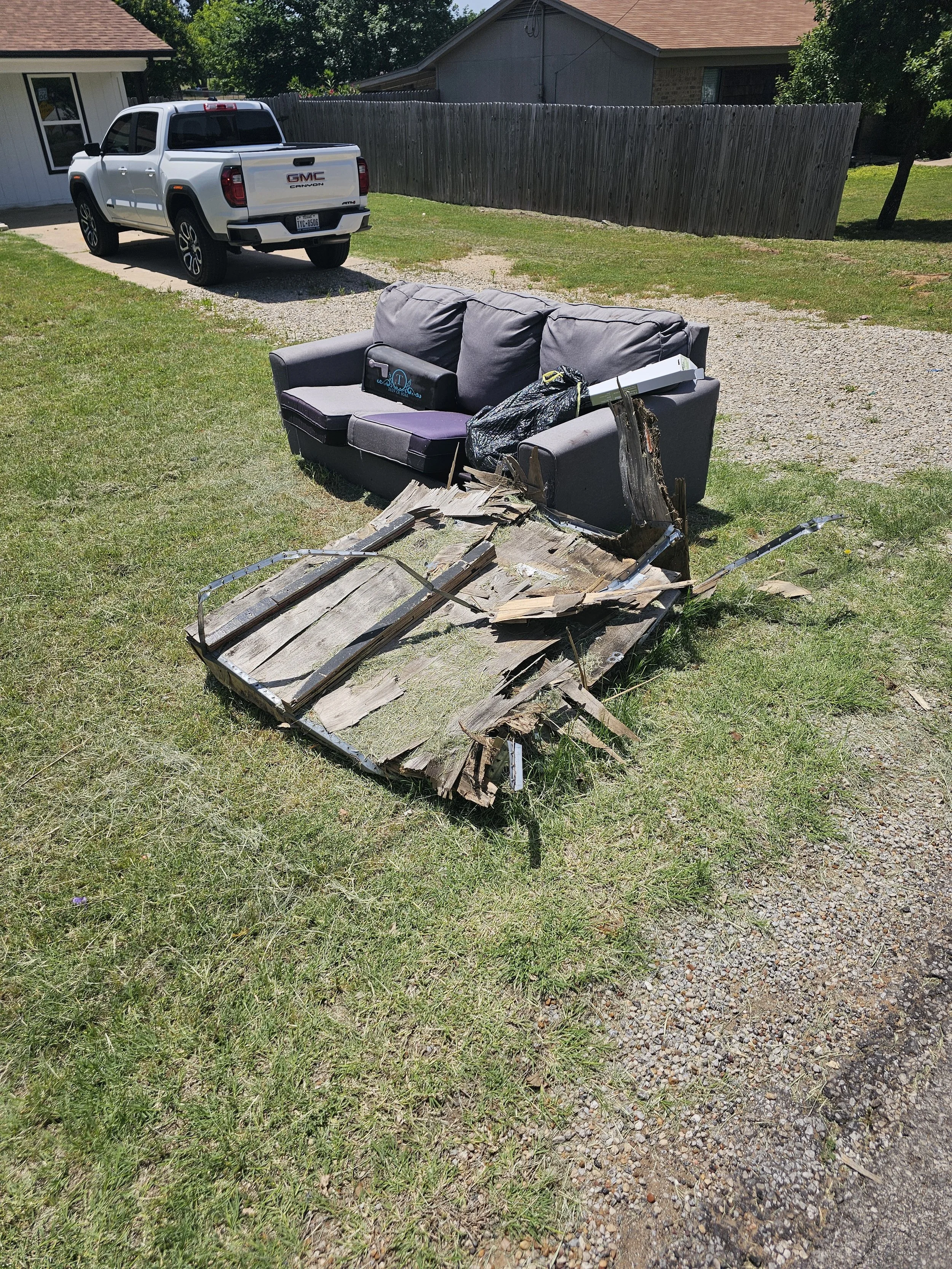 Layaway of damaged wooden furniture on grass, with a gray couch and a GMC pickup truck in the background in a residential yard.
