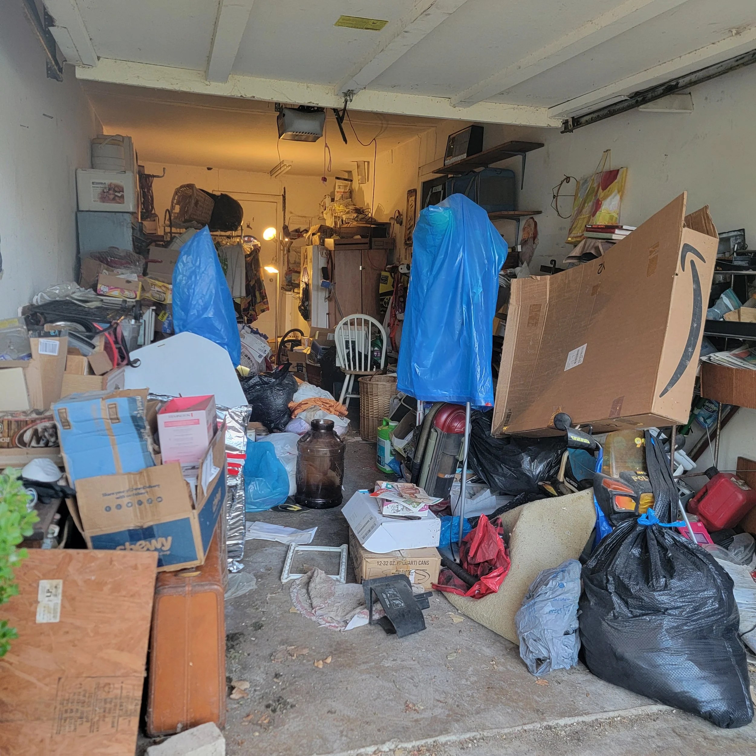 A cluttered garage filled with boxes, bags, and miscellaneous items scattered throughout.
