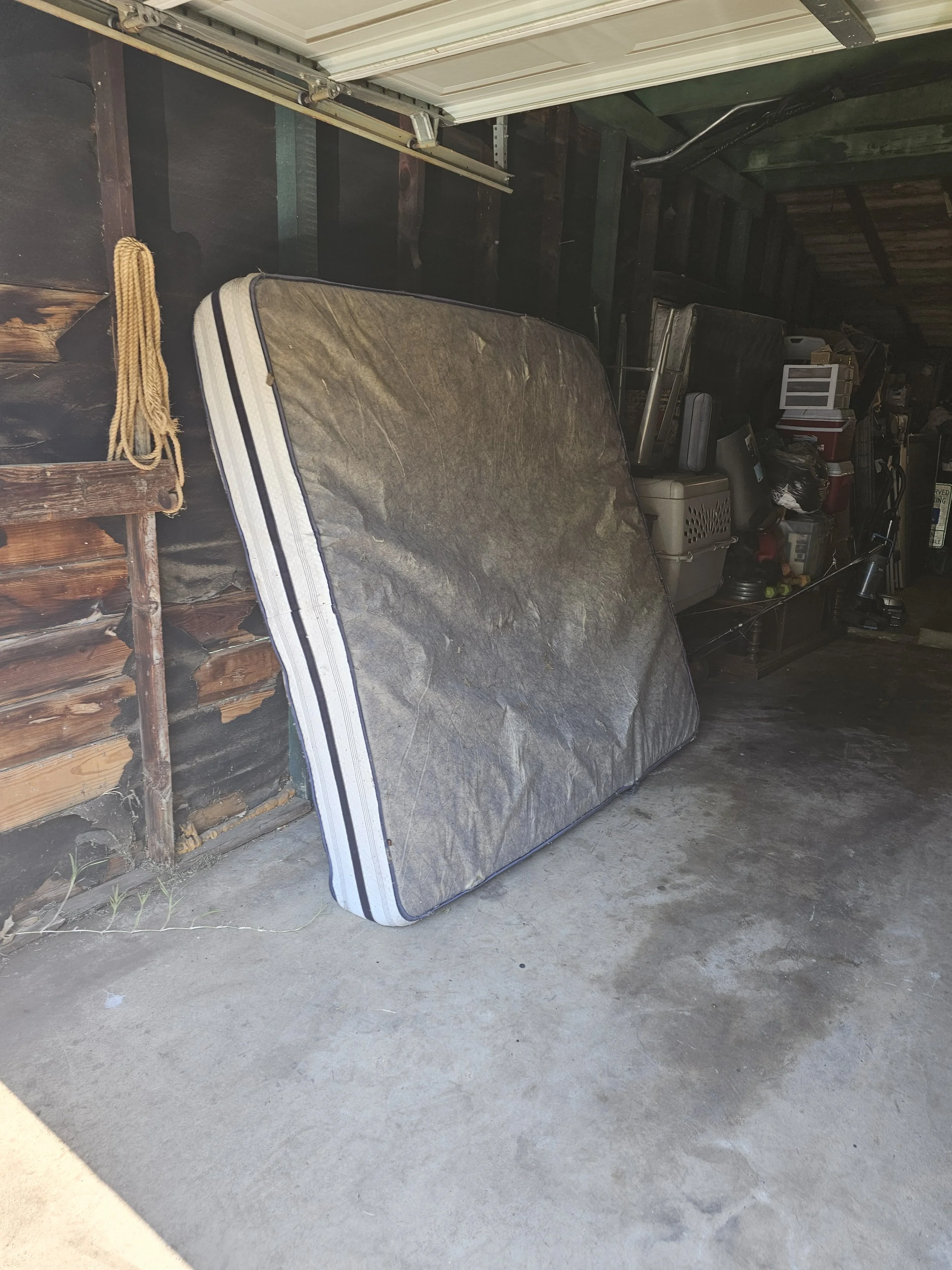 A mattress leaning against the interior wall of a cluttered garage, with various storage boxes