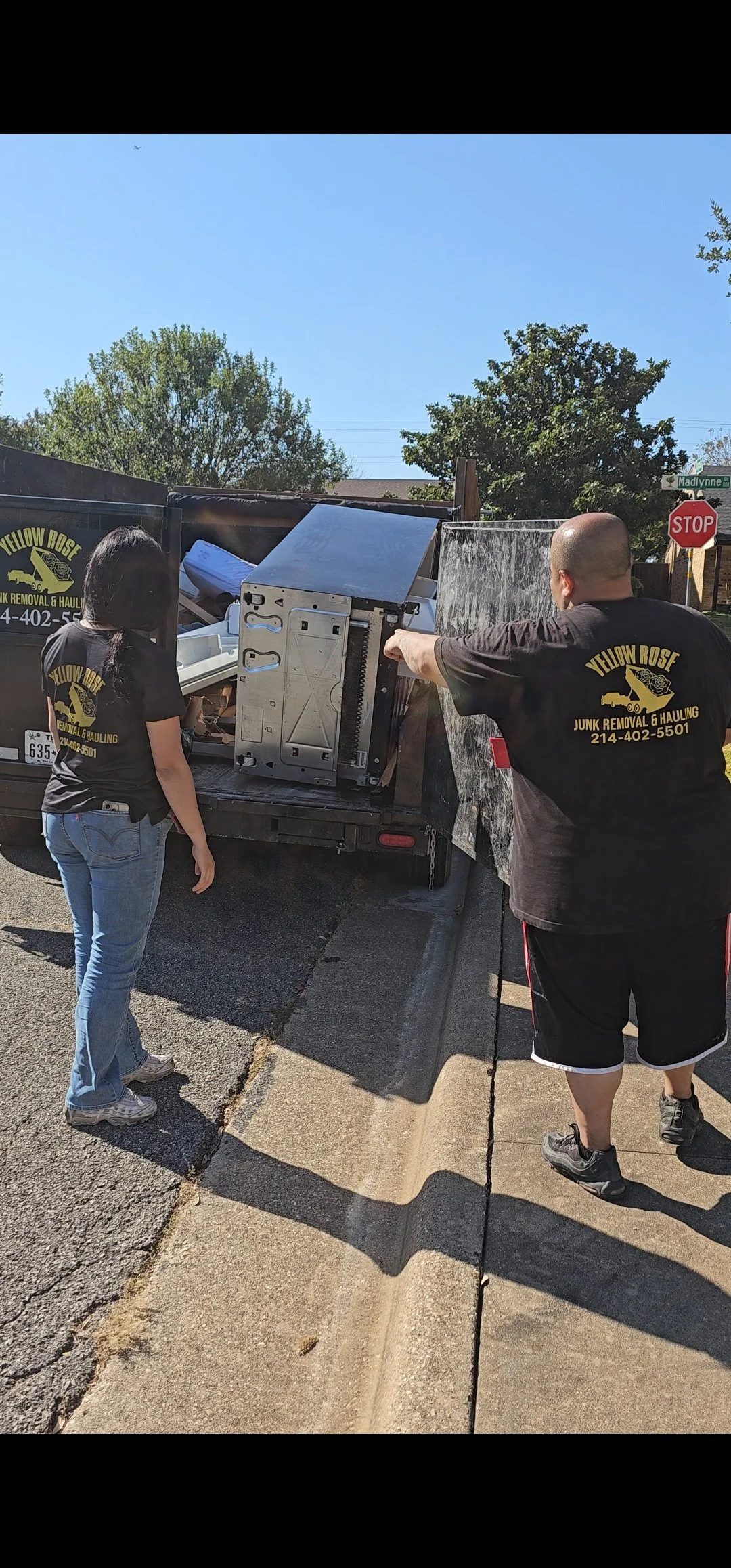 Dump Trailer being used for a property cleanout with two yellow Rose Junk Removal employees nearby.