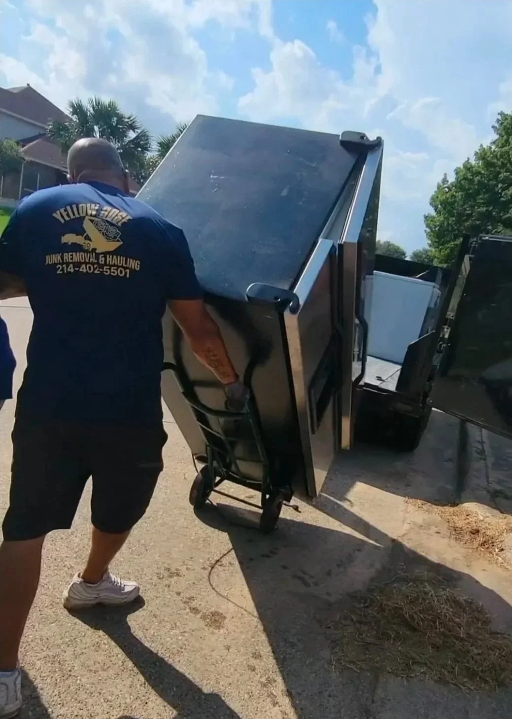 Man moving a large black refrigerator or appliance with a hand truck in Dallas.