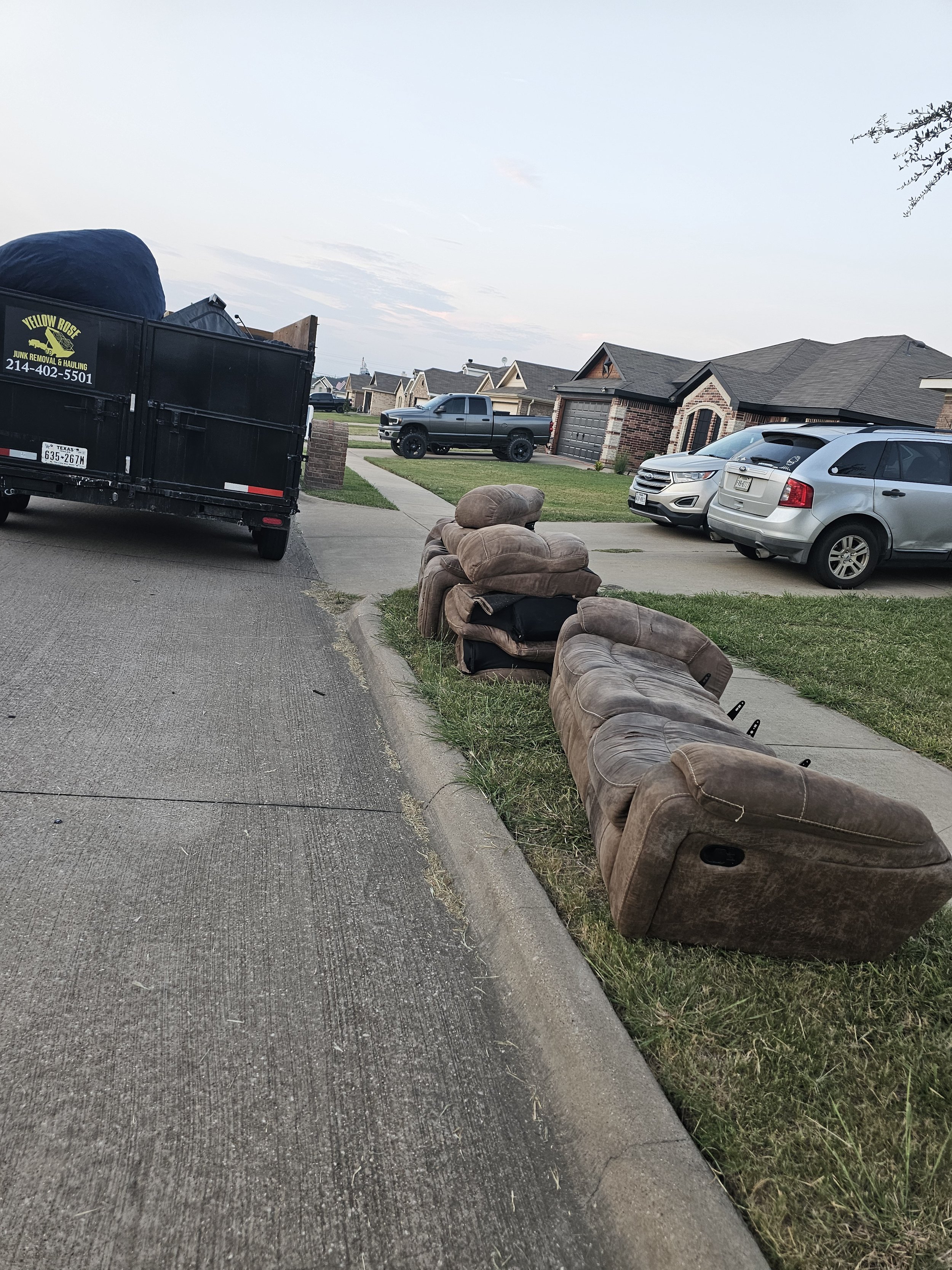 furniture disposal on the sidewalk with old couches and recliners lined up outside a suburban home, with a trash trailer nearby.