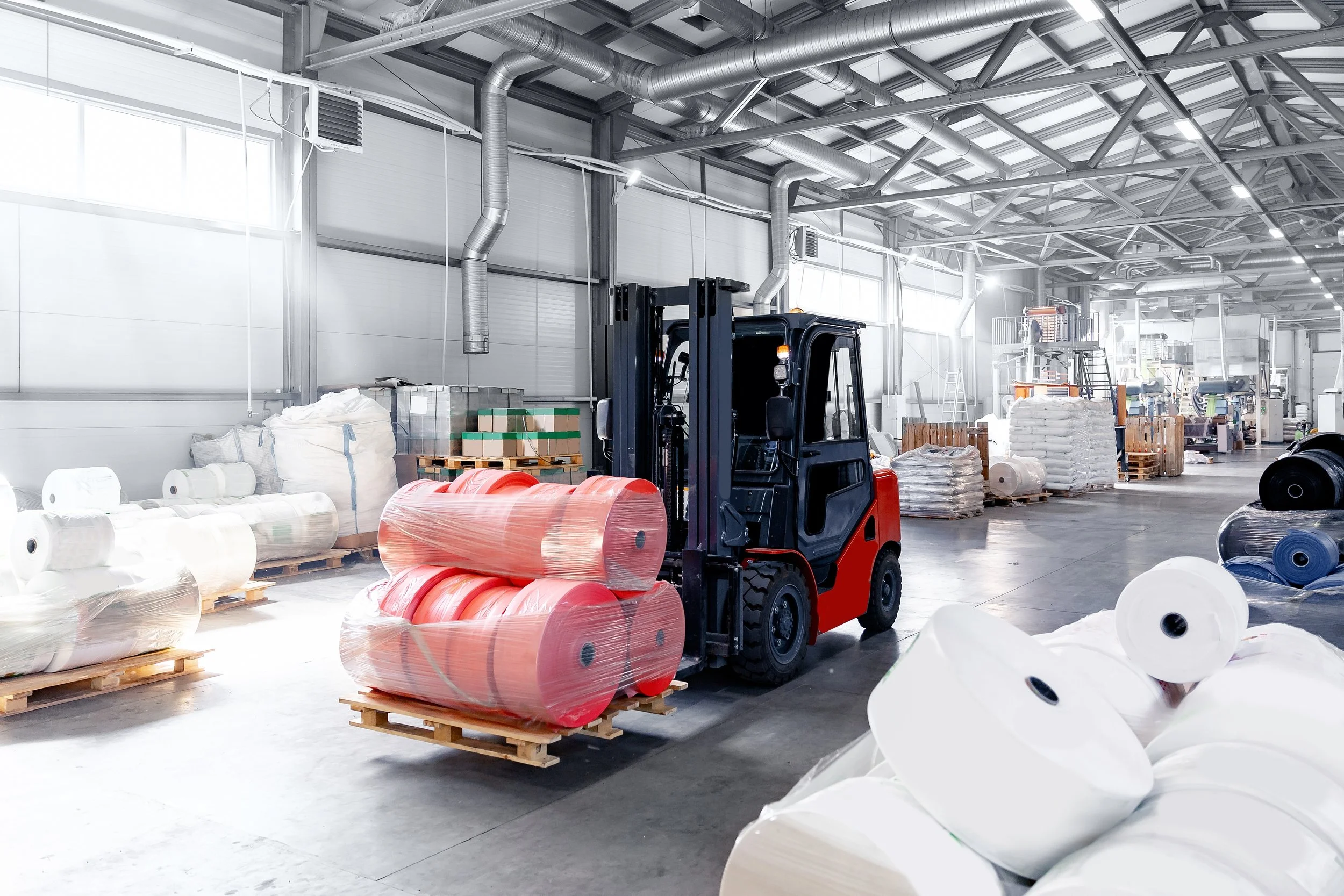 Forklift moving palletized rolls of plastic film inside an industrial warehouse