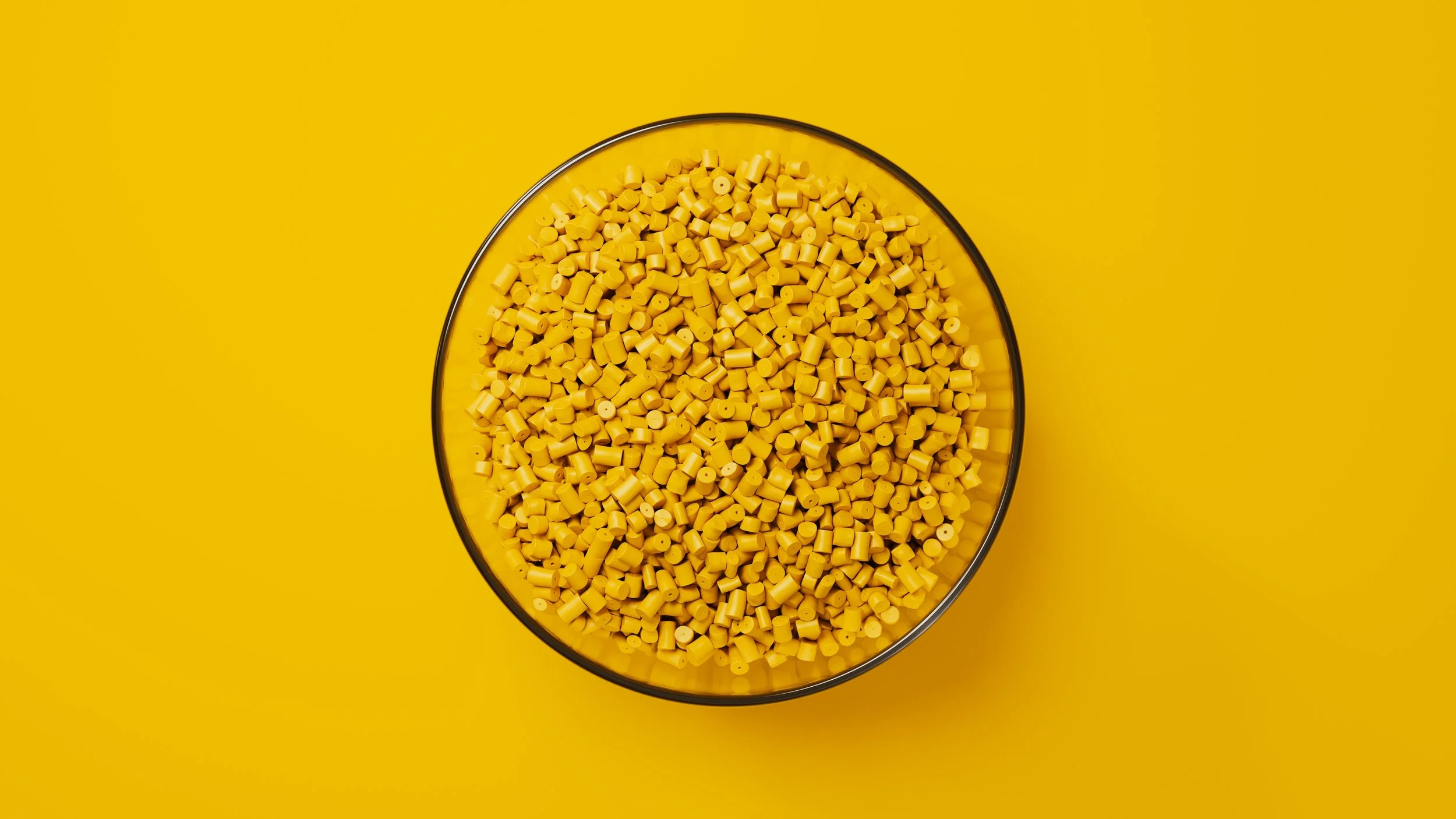 Overhead view of a glass bowl filled with yellow cylindrical beads on a yellow background