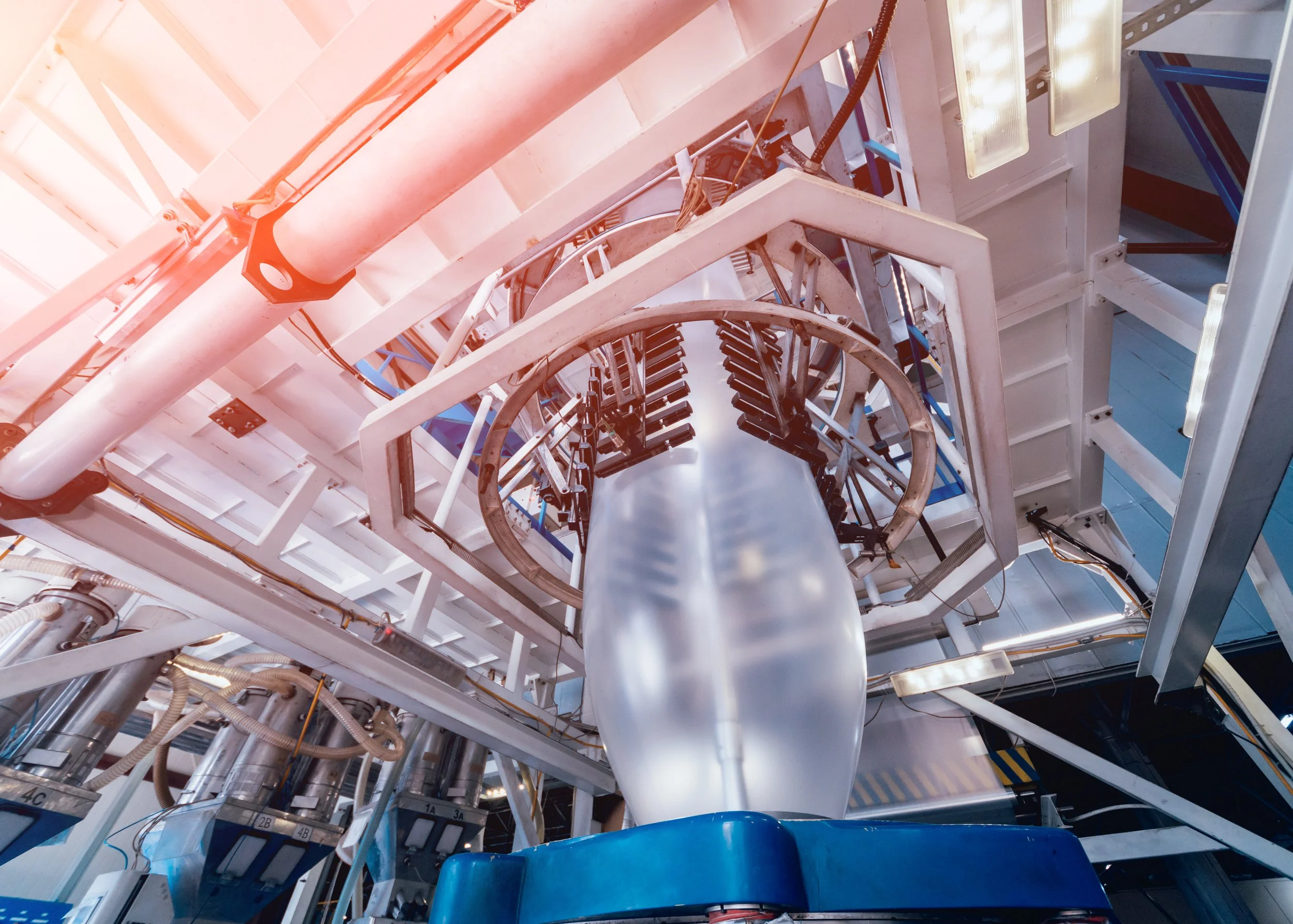 Interior of an industrial manufacturing machine with large white rollers, metal frames, cables, and blue components