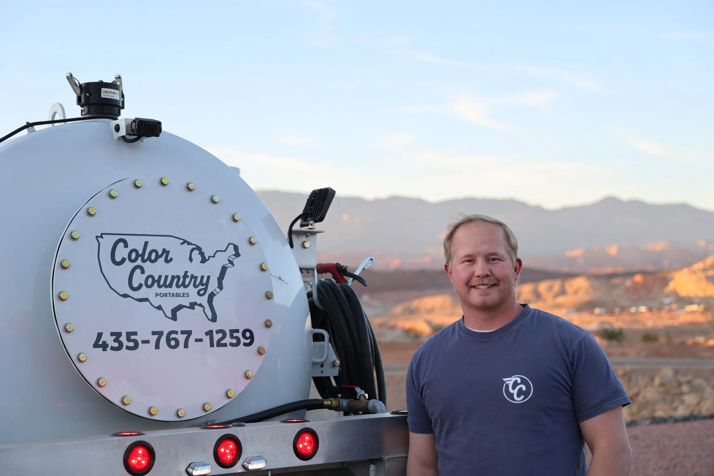 Garret Hafen, owner of Color Country Portables, standing outside next to a large truck labeled 'Color Country Portables' in a desert landscape with mountains in the background during sunset.