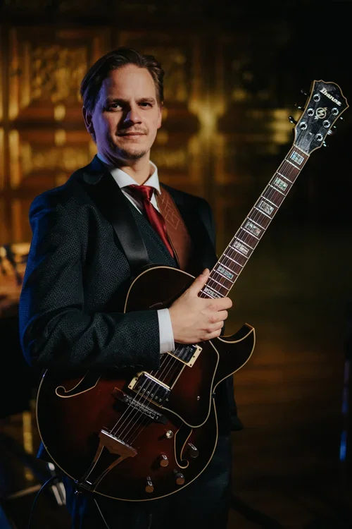 A man in a suit holding an electric guitar in a dimly lit room.