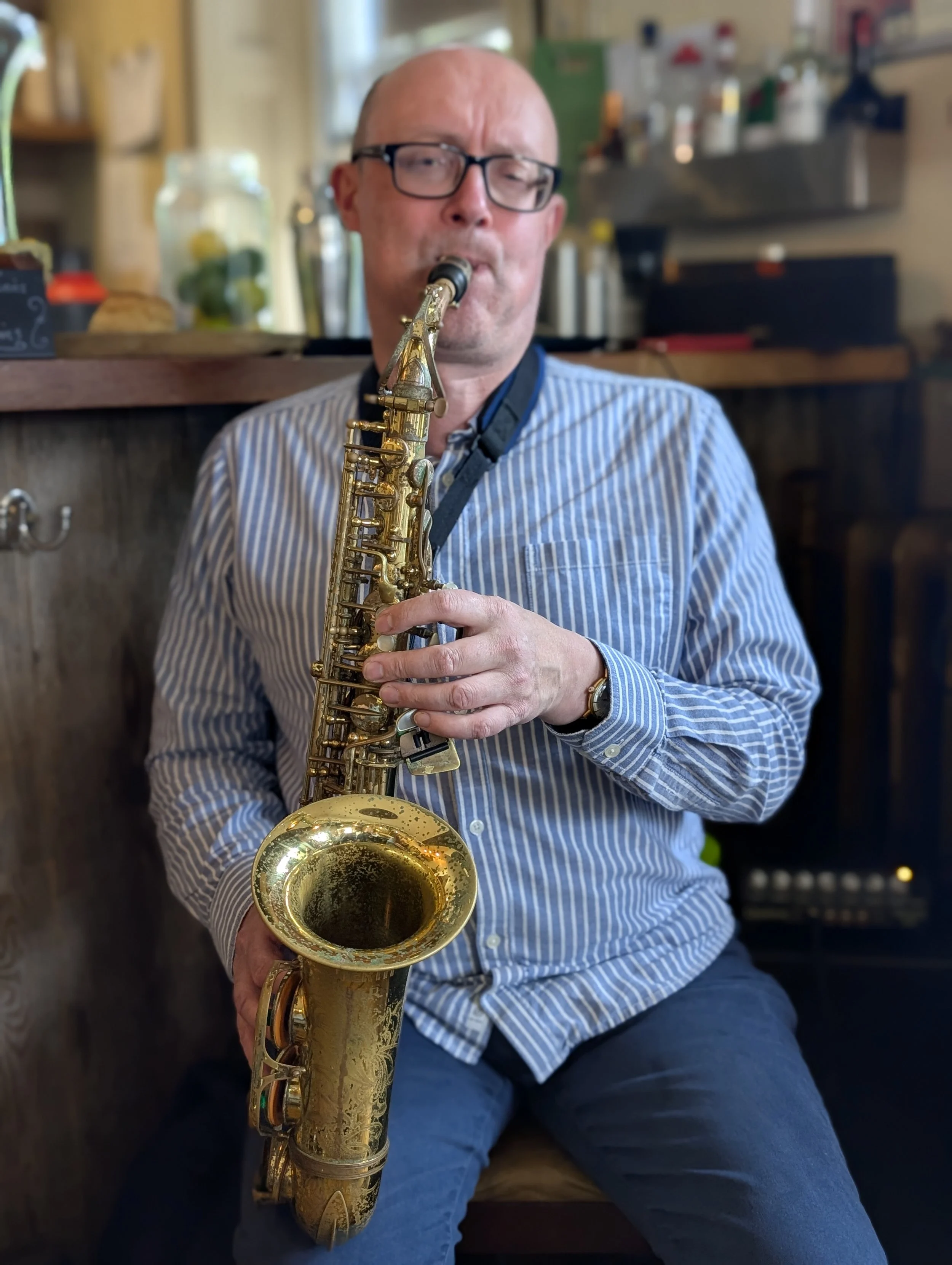 A man with glasses and a striped shirt playing a gold saxophone.