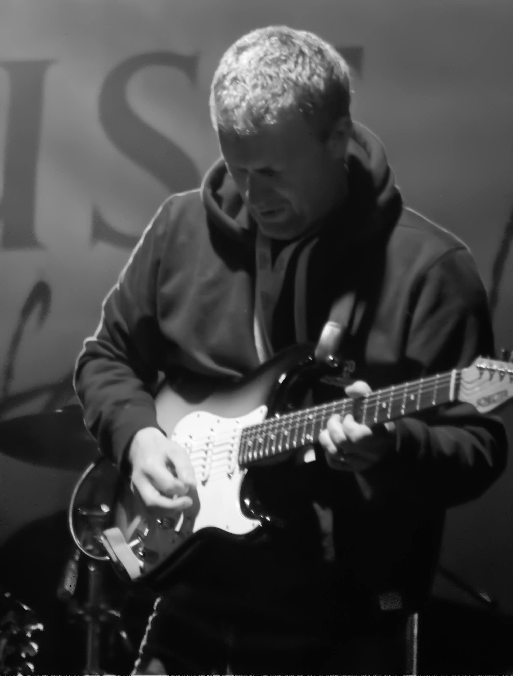 A person playing an electric guitar on stage, with a focused expression.