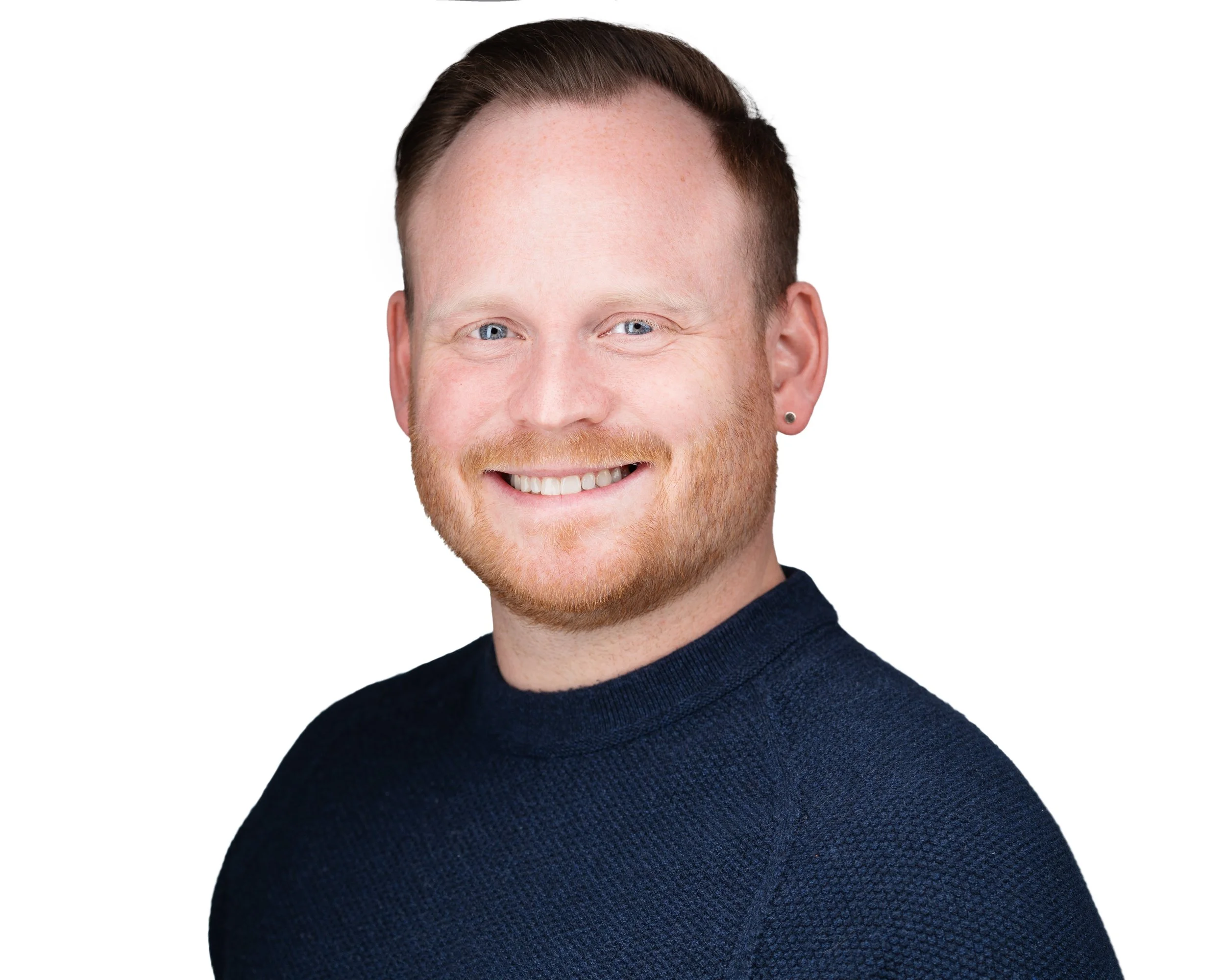 Headshot of a man with red hair, blue eyes, and a beard, smiling and wearing a dark blue sweater, against a white background.