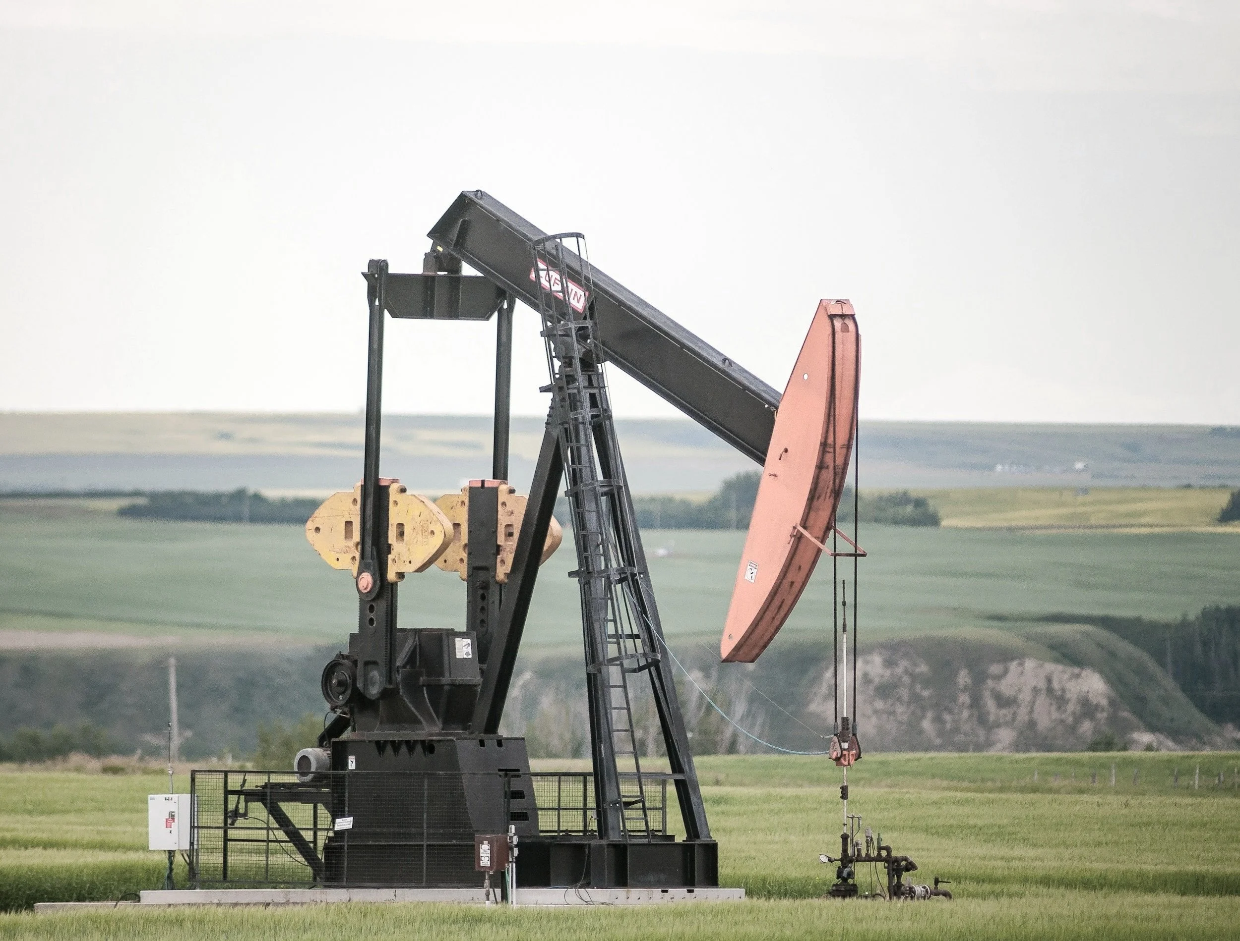 Oil pumpjack operating in a green field with rolling hills in the background.