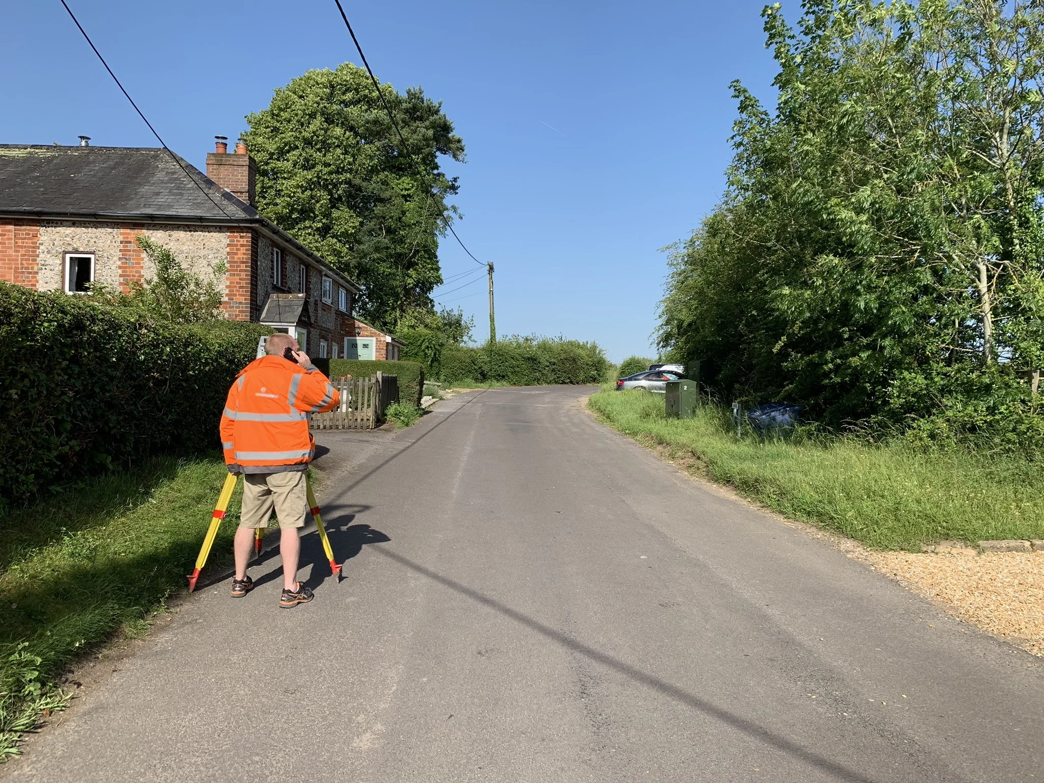 Surveyor using surveying equipment beside the road to check levels for Hill Top House, Dummer, Hampshire.