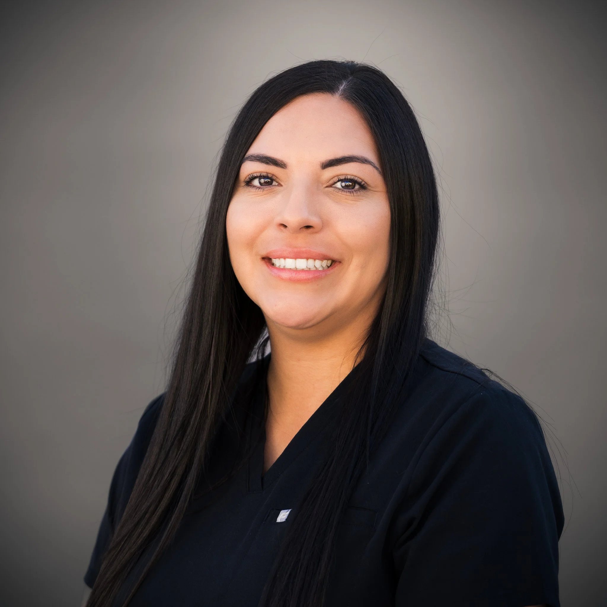 Portrait of a woman with long, wavy hair wearing a black top, against a beige background.