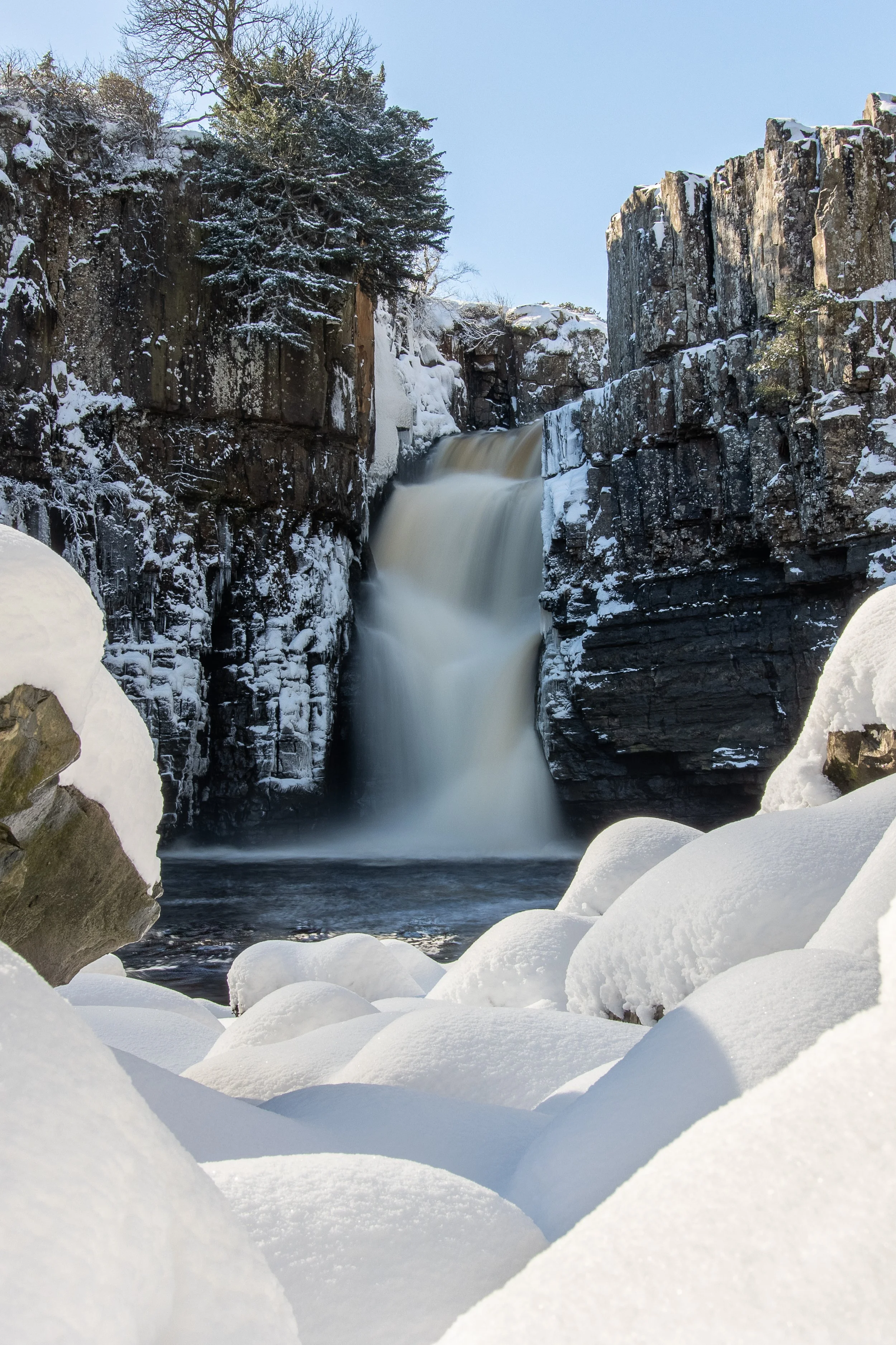 Snow-covered rocky landscape with a waterfall cascading between cliffs.