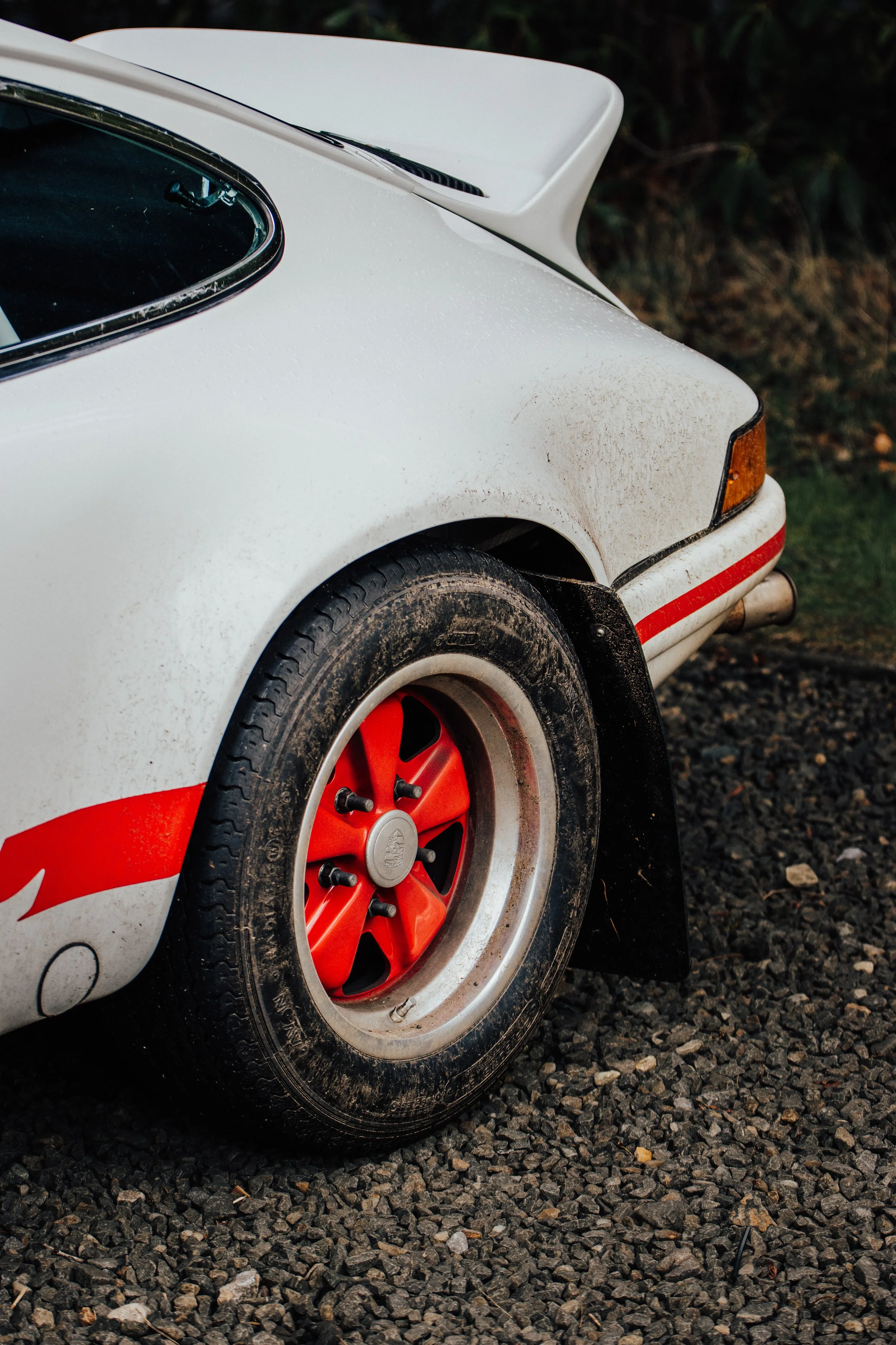 Close-up of a classic sports car with white body, red stripe and rim, and a rear spoiler.
