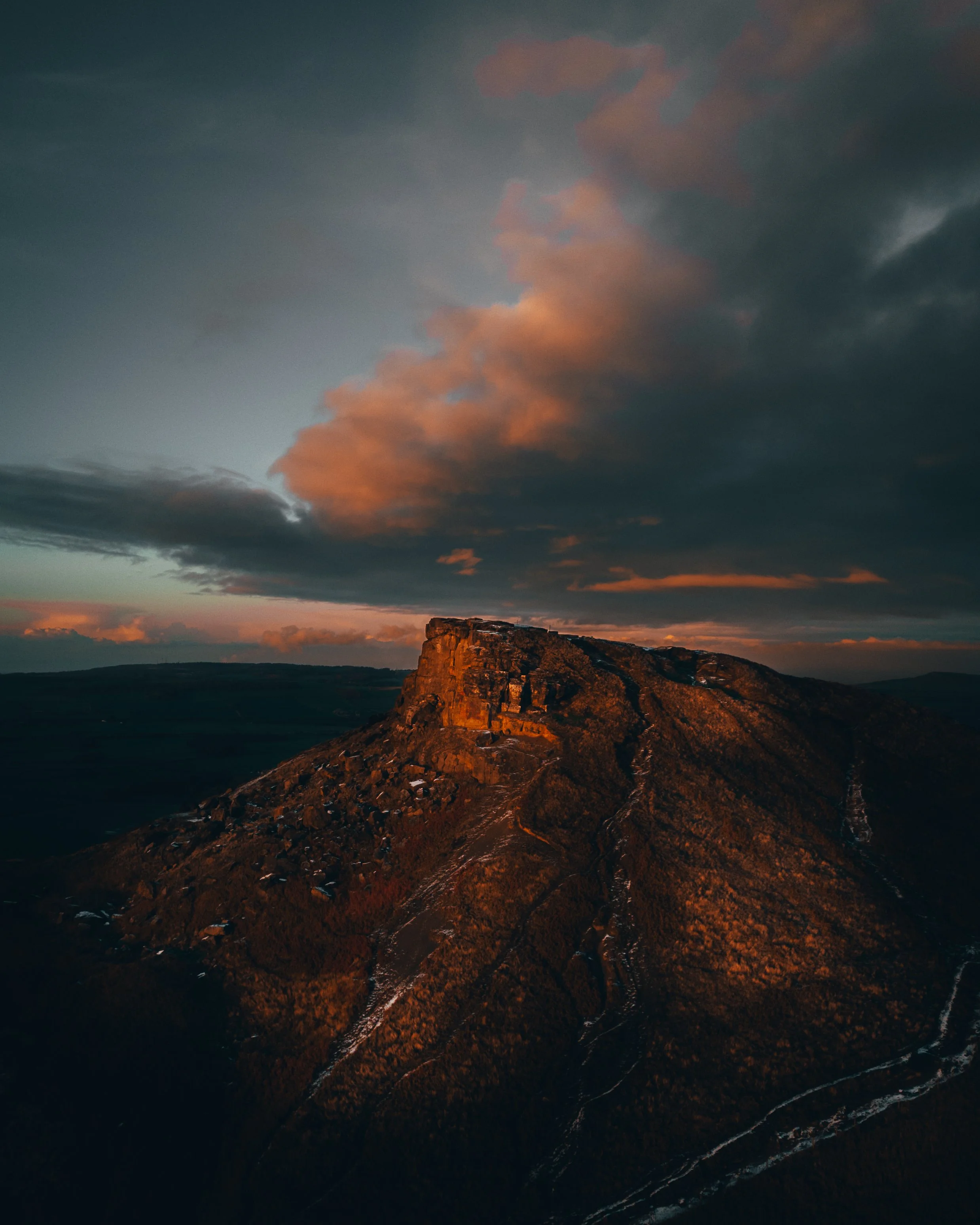 Aerial view of a mountain peak during sunset with dramatic clouds in the sky.