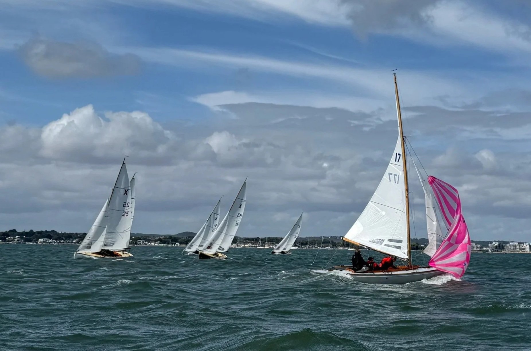 Sailboats racing on the water with a cloudy sky and distant shoreline in the background.