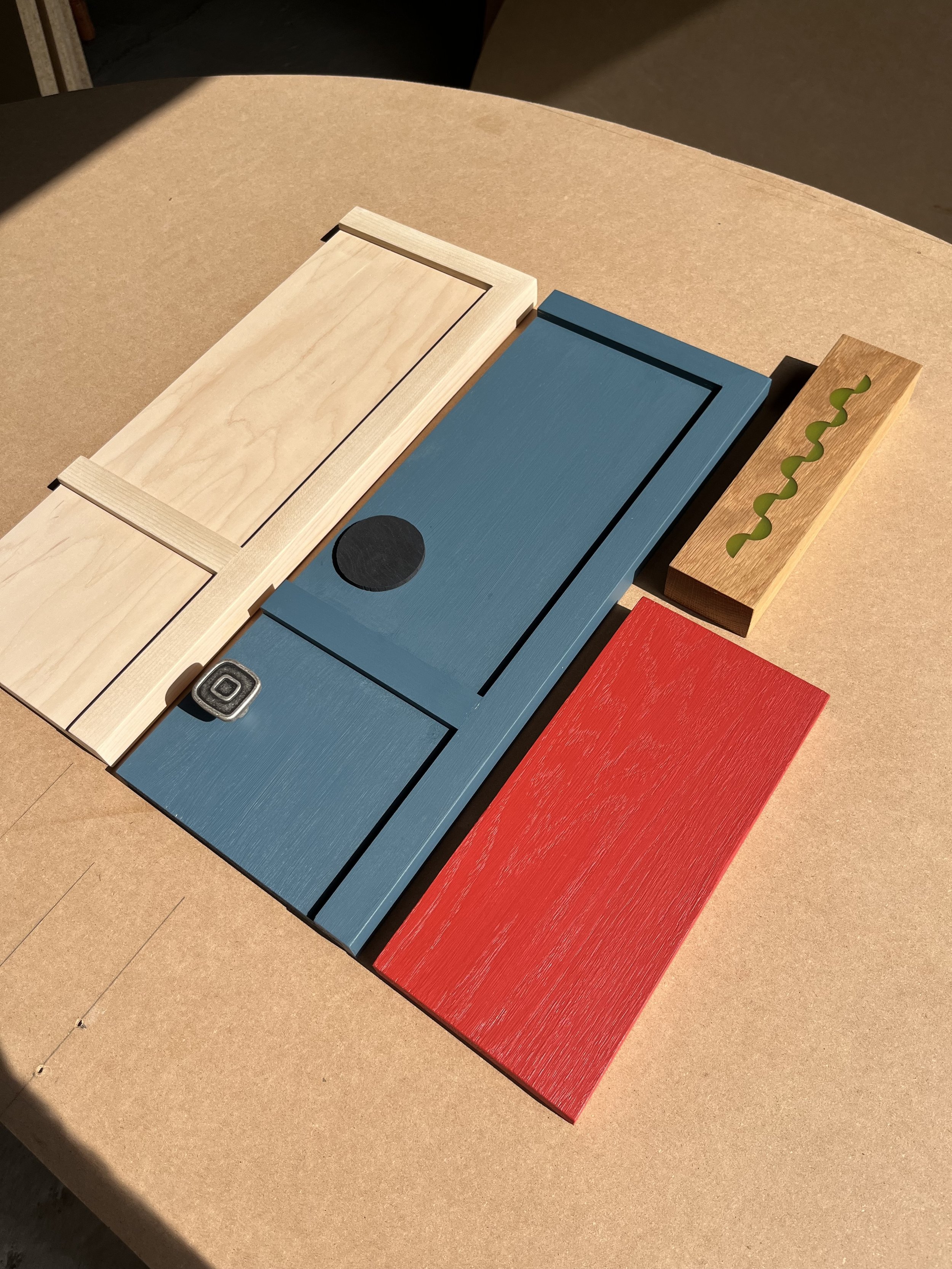 Arrangement of colorful wooden blocks on a cardboard surface, including natural, blue, red, and tan with green accents.