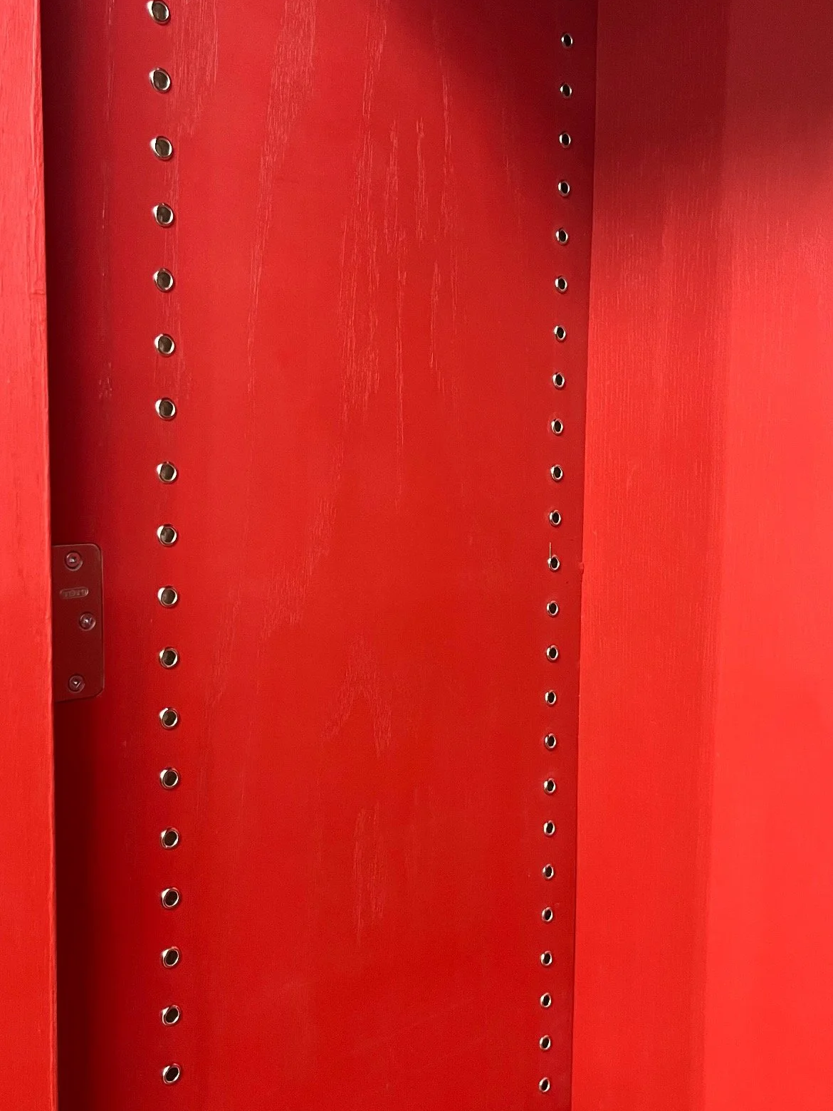 Empty red shelving unit with adjustable metal pegs for shelves.