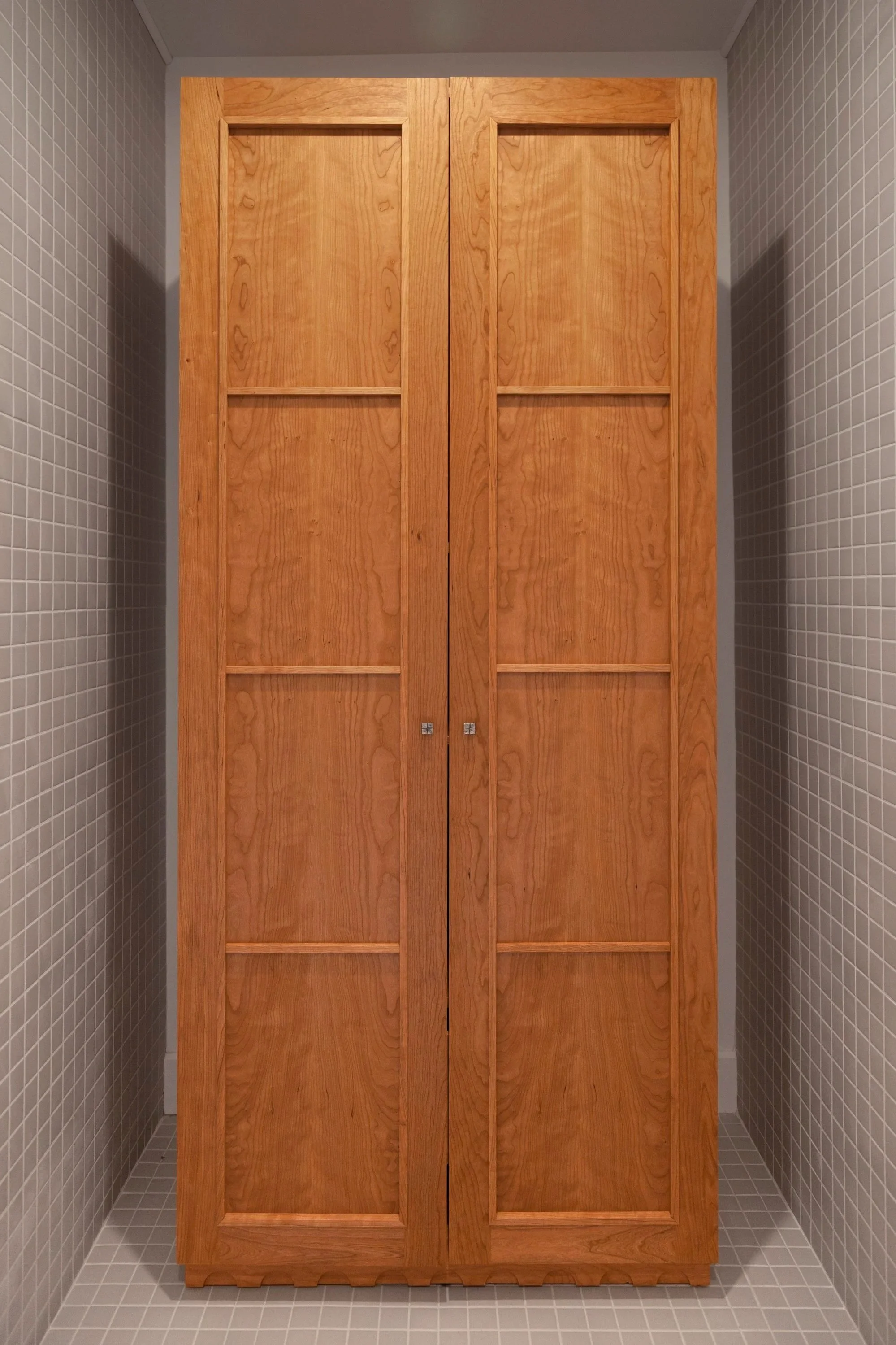 Wooden cabinet with double doors in a small tiled room or closet.