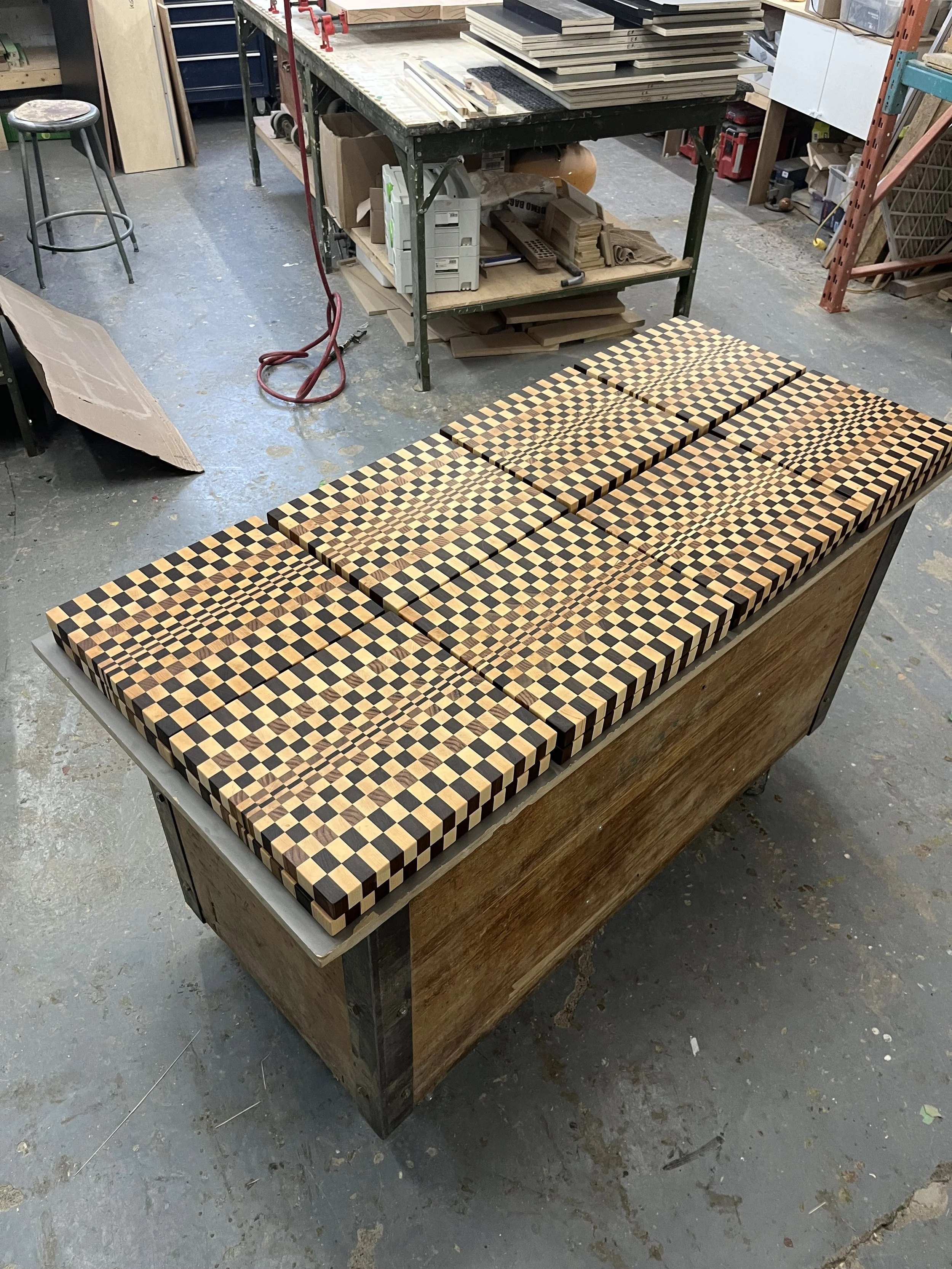 A woodworking workbench with multiple pieces of mitered wooden boards arranged for a pattern, surrounded by various tools and materials in a workshop setting.