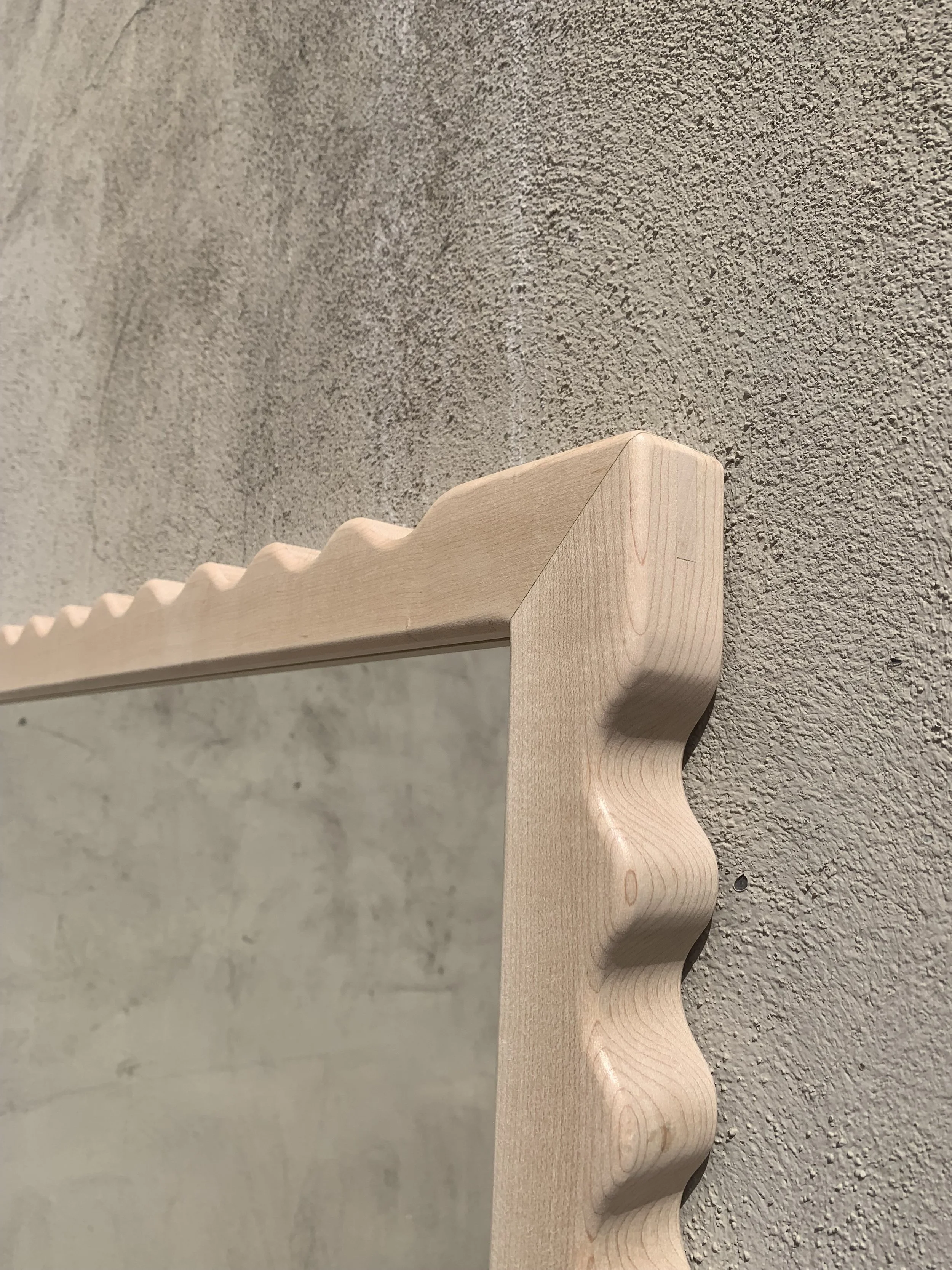 Close-up of a wooden mirror frame with a scalloped edge design, mounted on a textured beige wall.