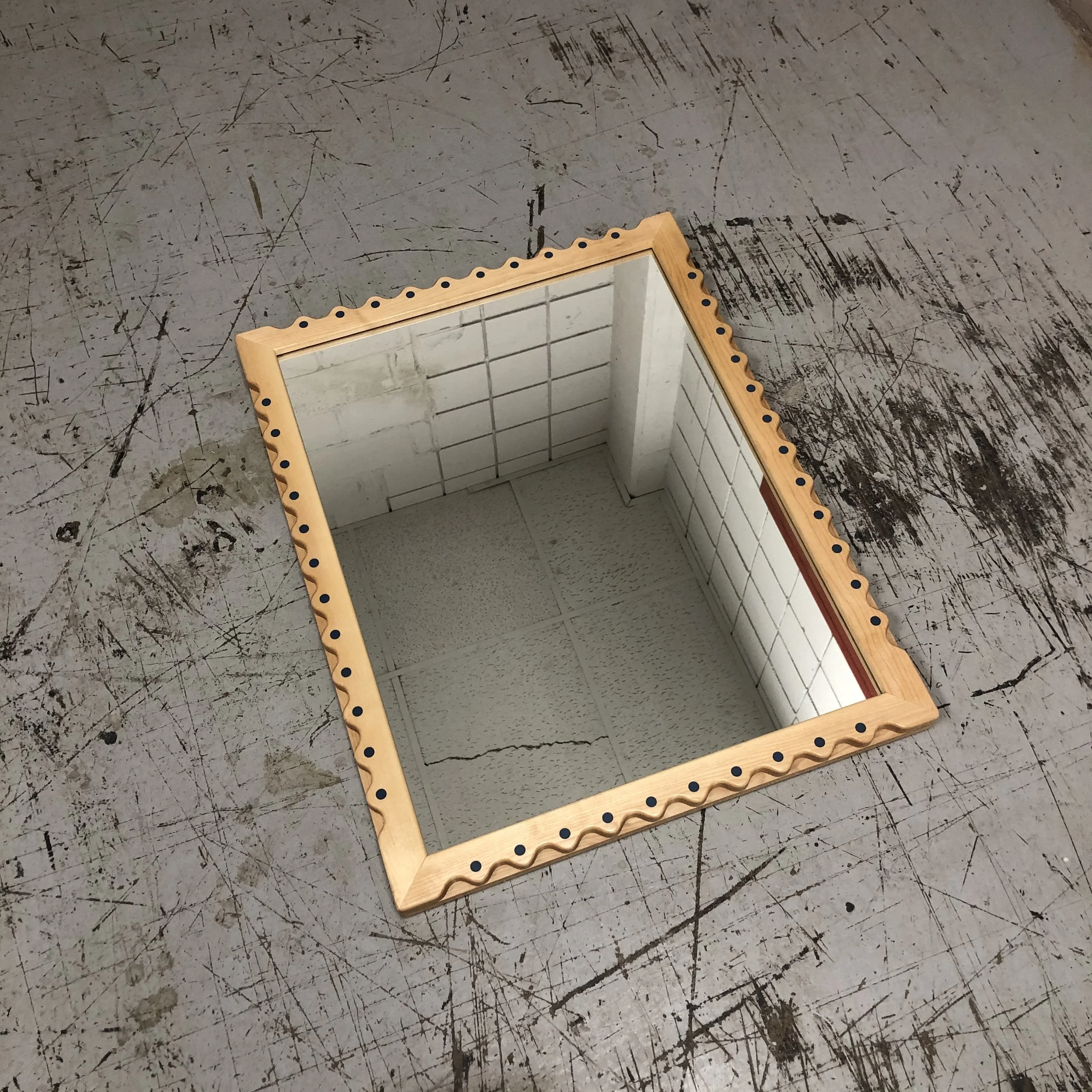A rectangular mirror with a wooden frame and decorative holes is placed on a scratched and worn industrial metal surface.