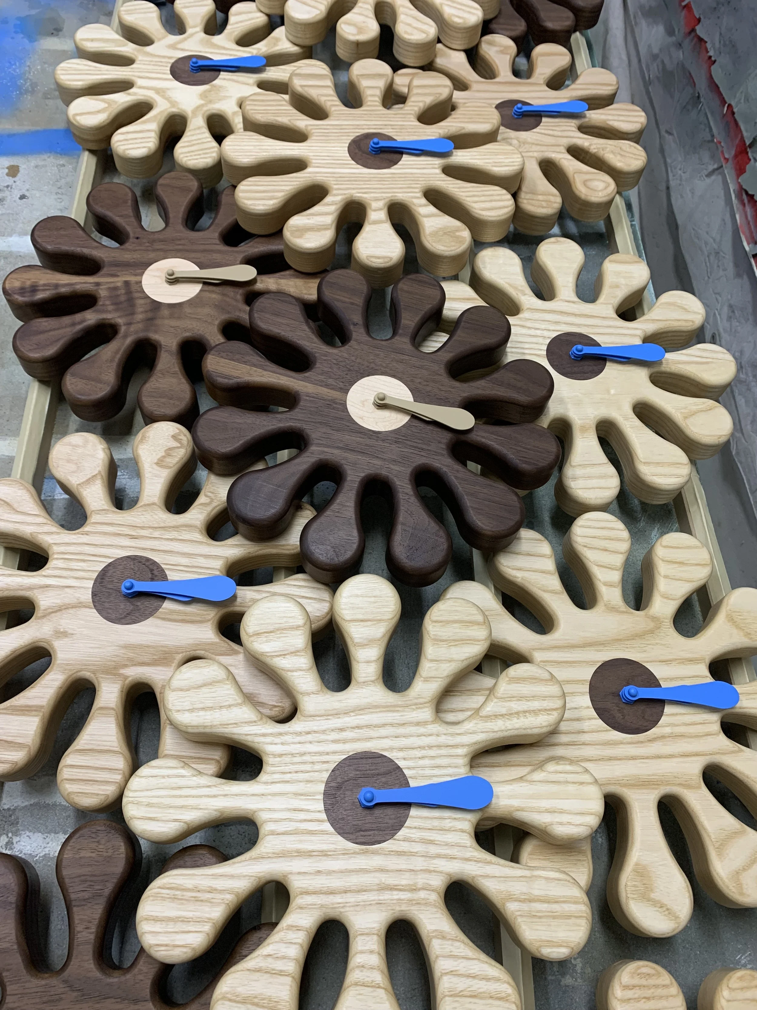 Multiple wooden snowflake-shaped clocks with blue and beige hands, arranged on a surface.