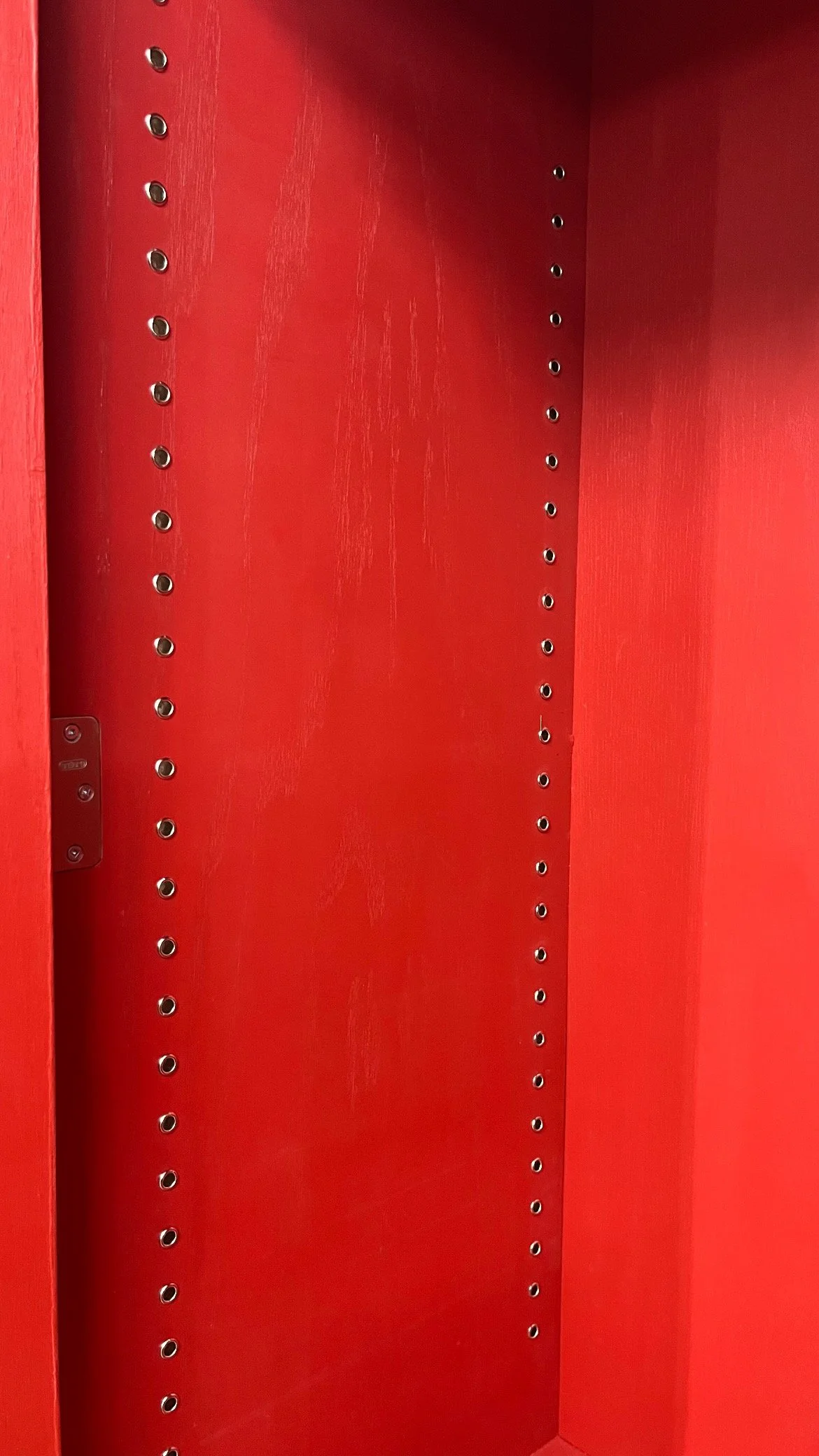 Empty red shelving unit with adjustable metal pegs for shelves.