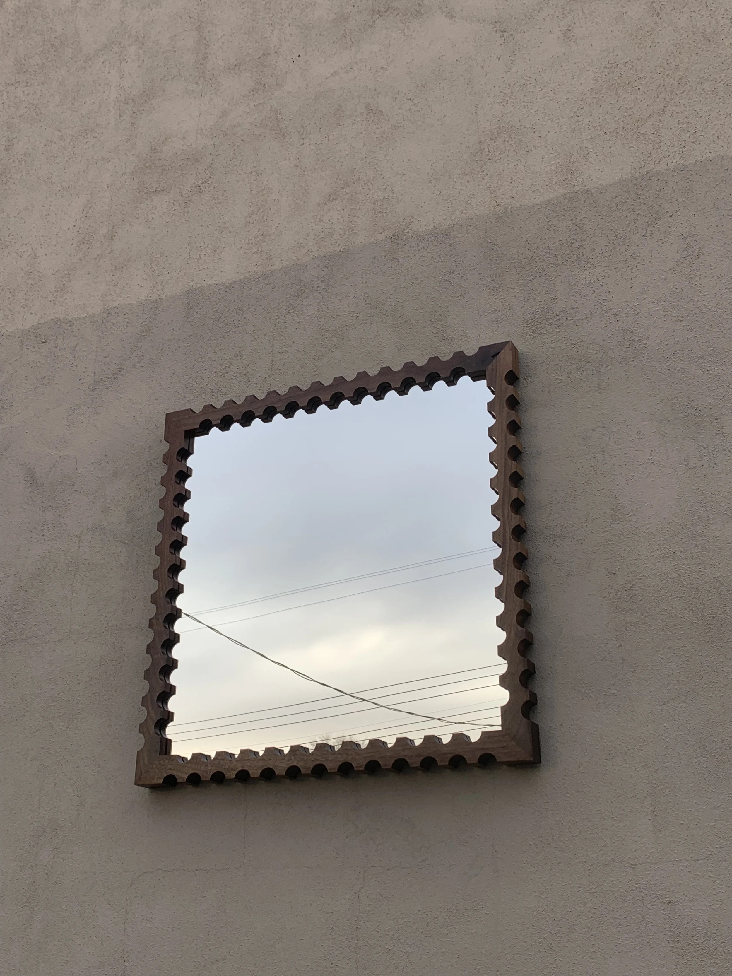 Square window with a decorative wooden frame, showing a cloudy sky and power lines outside.
