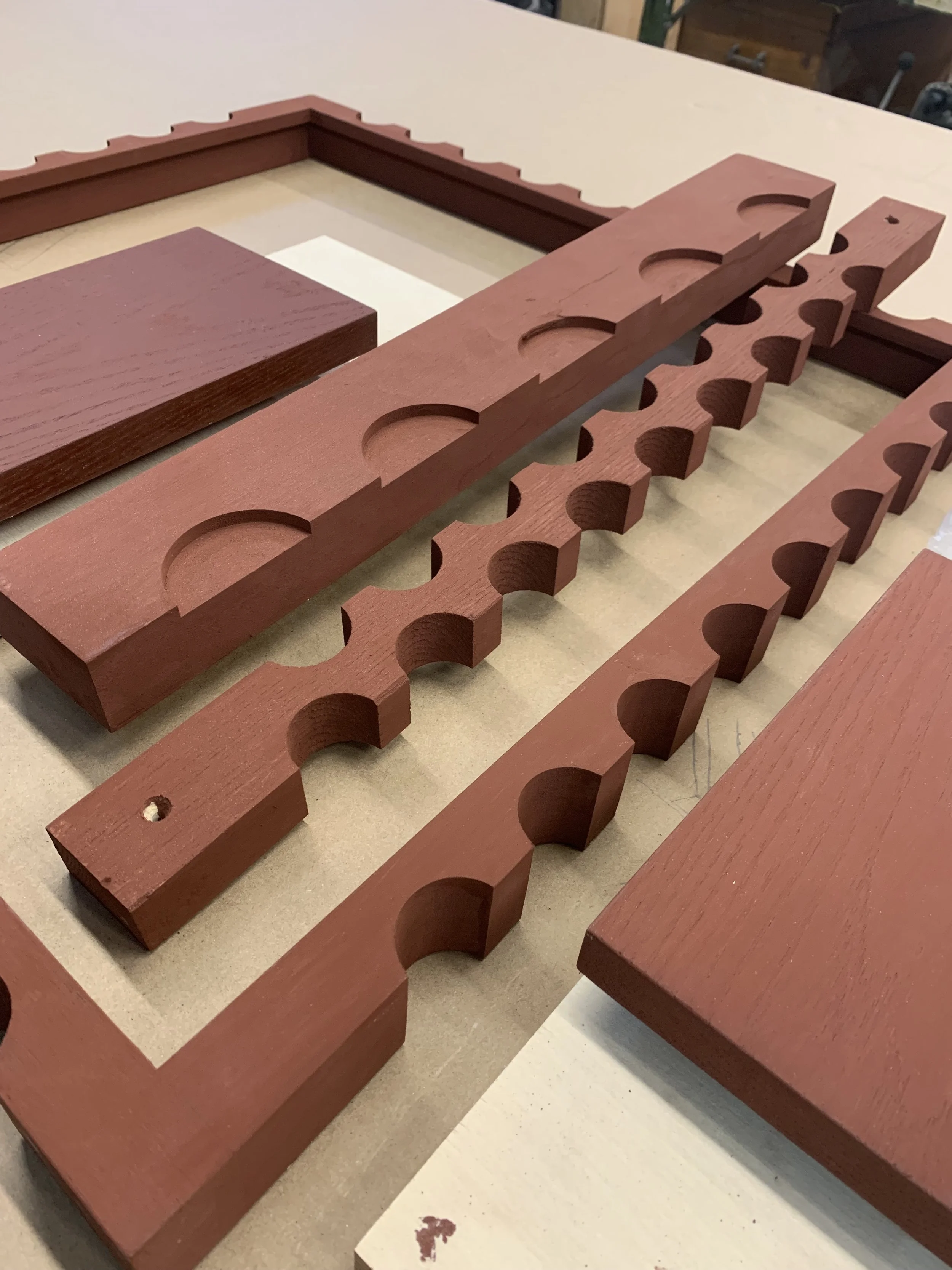 Multiple red wooden frame parts with semicircular cutouts and notches laid out on a workspace.