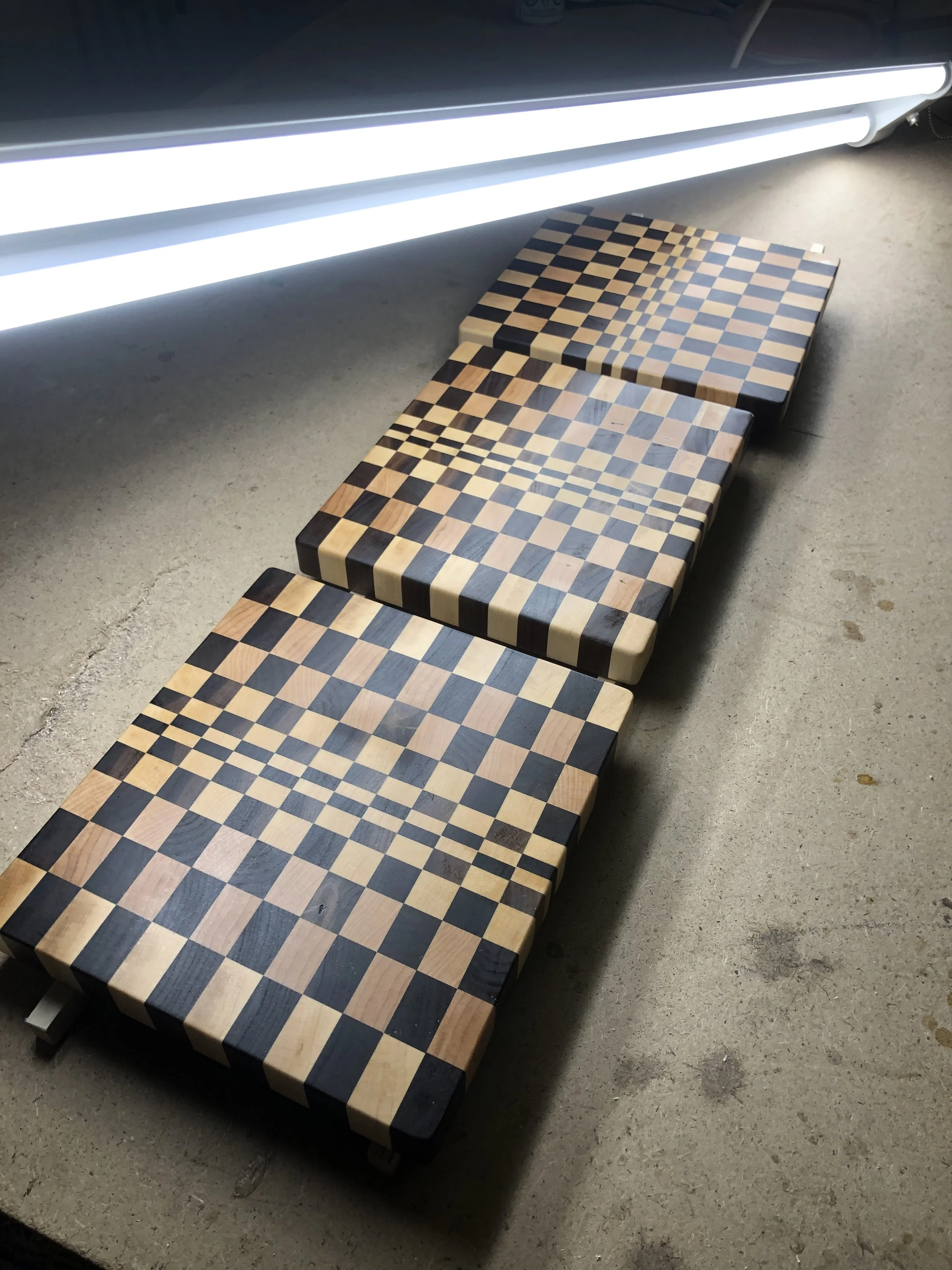 Three wooden benches with chessboard patterns on the seats are arranged in a row on a concrete floor, with fluorescent lights overhead.