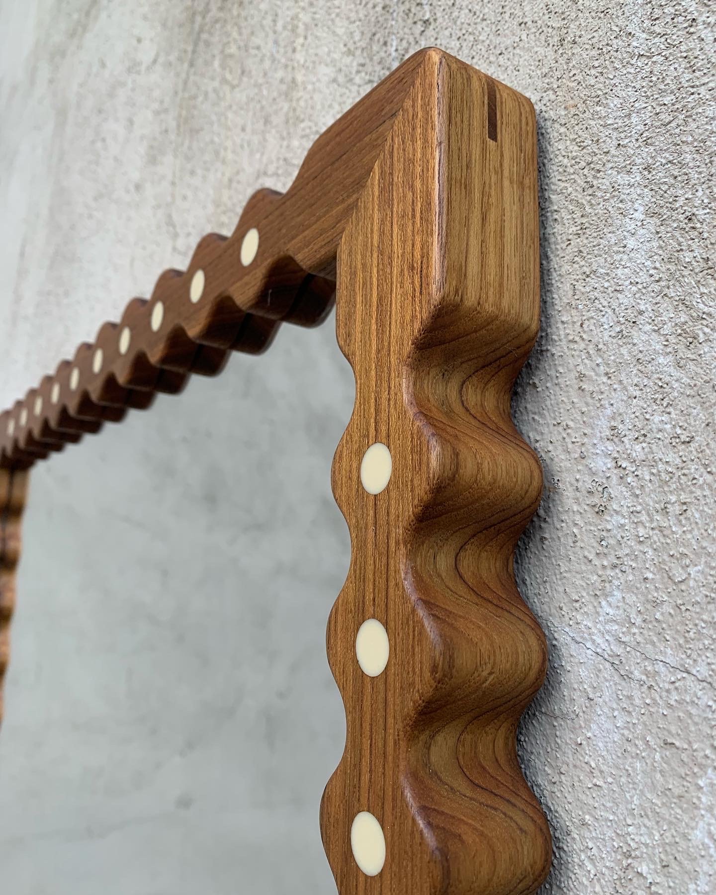 Close-up of a wavy wooden picture frame with cream-colored fasteners, mounted on a textured white wall.